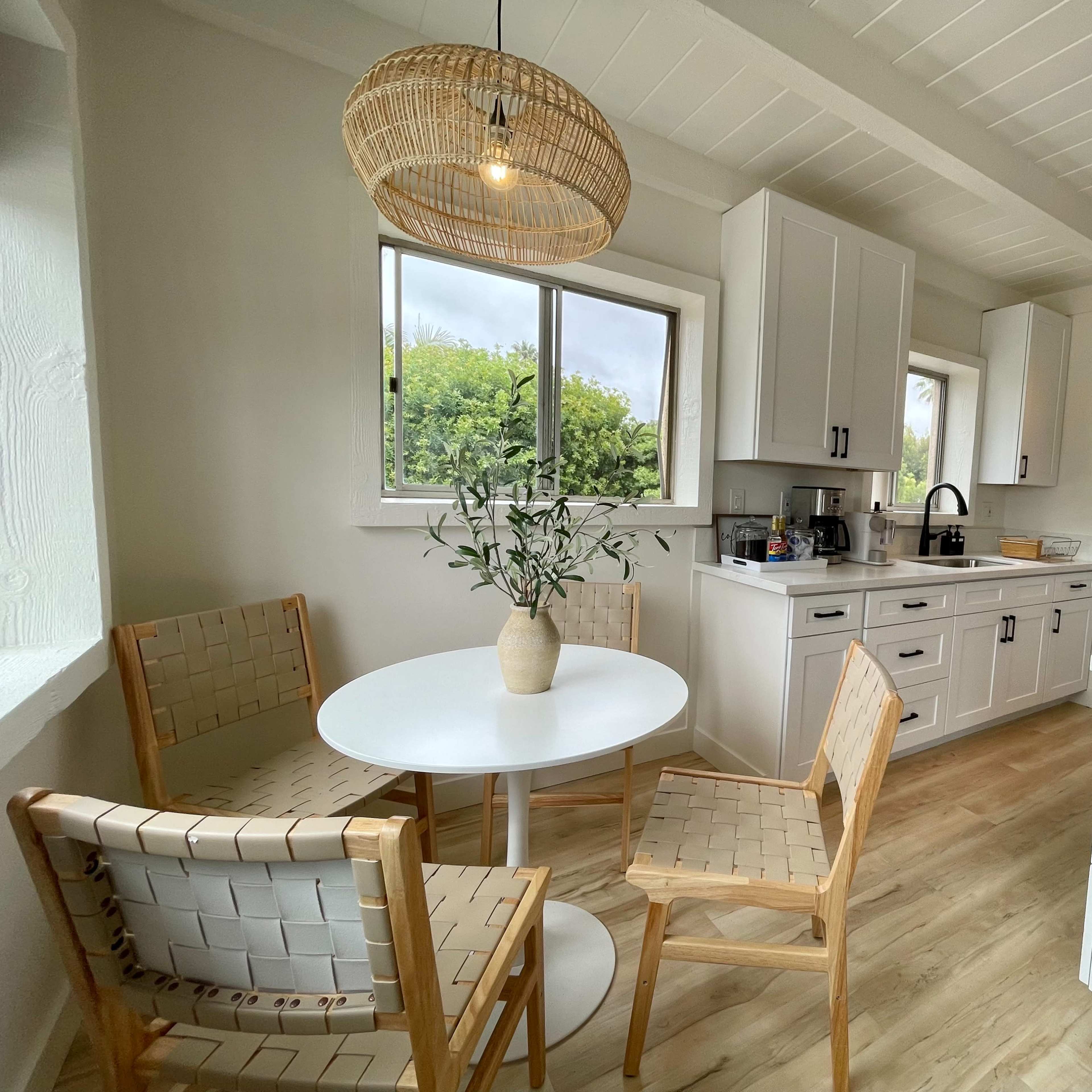 A cozy kitchen with a round dining table surrounded by two wooden chairs and two woven chairs, featuring white cabinets and a black stove.