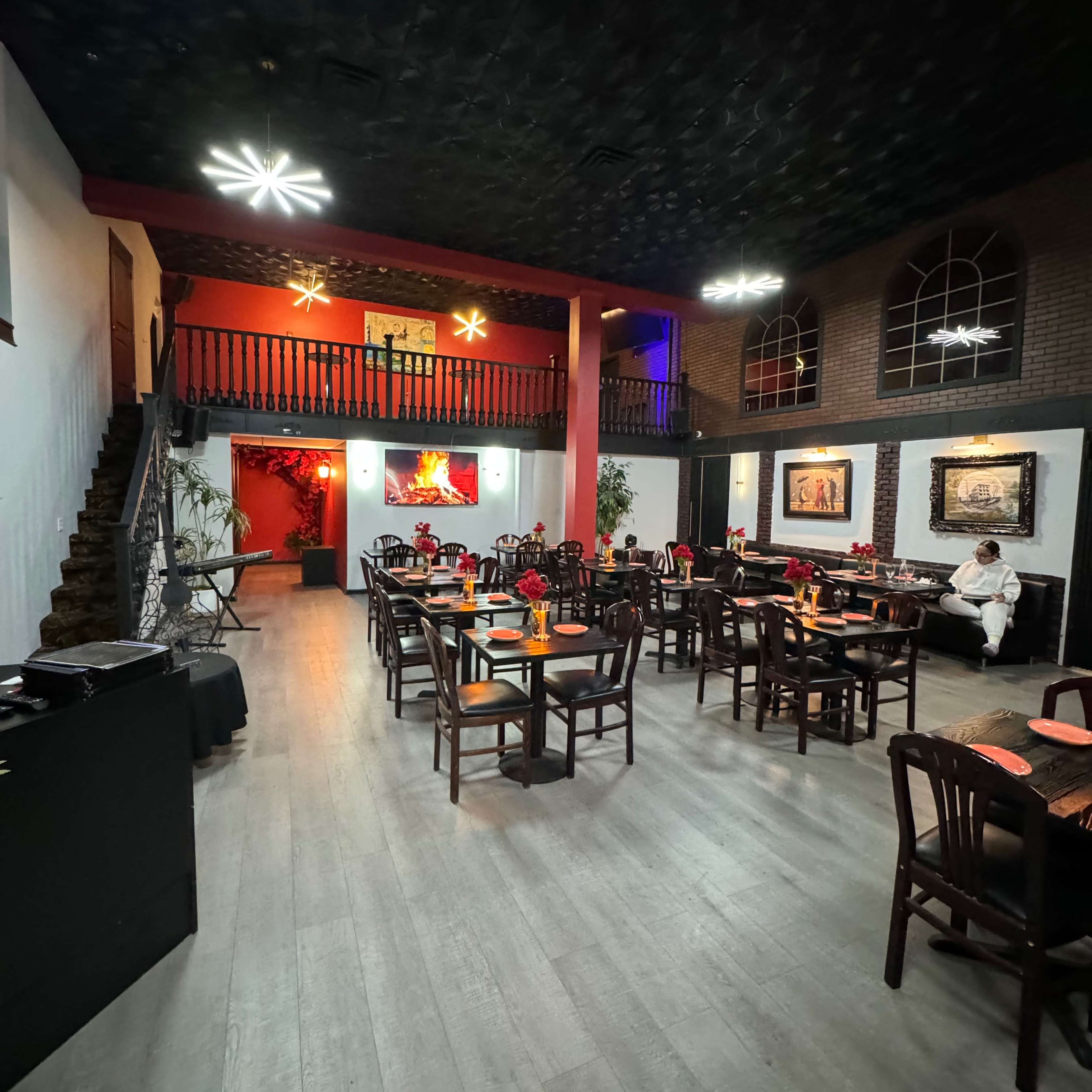 A spacious restaurant with several wooden tables set for dining, a staircase in the background, and decorative lighting fixtures on the ceiling.