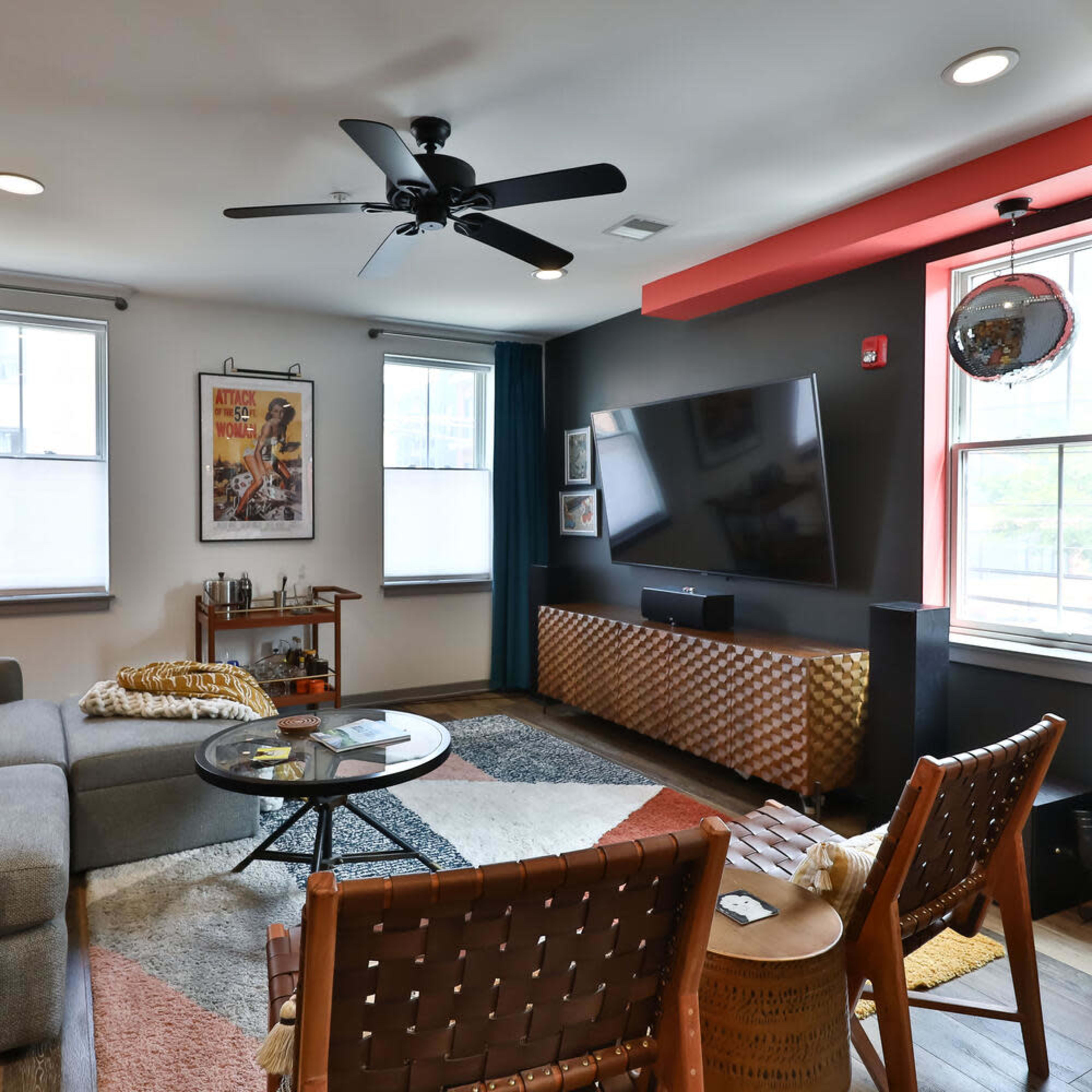 A modern living room with a gray sectional sofa, a large wall-mounted TV, and a combination of colorful decor and furniture.