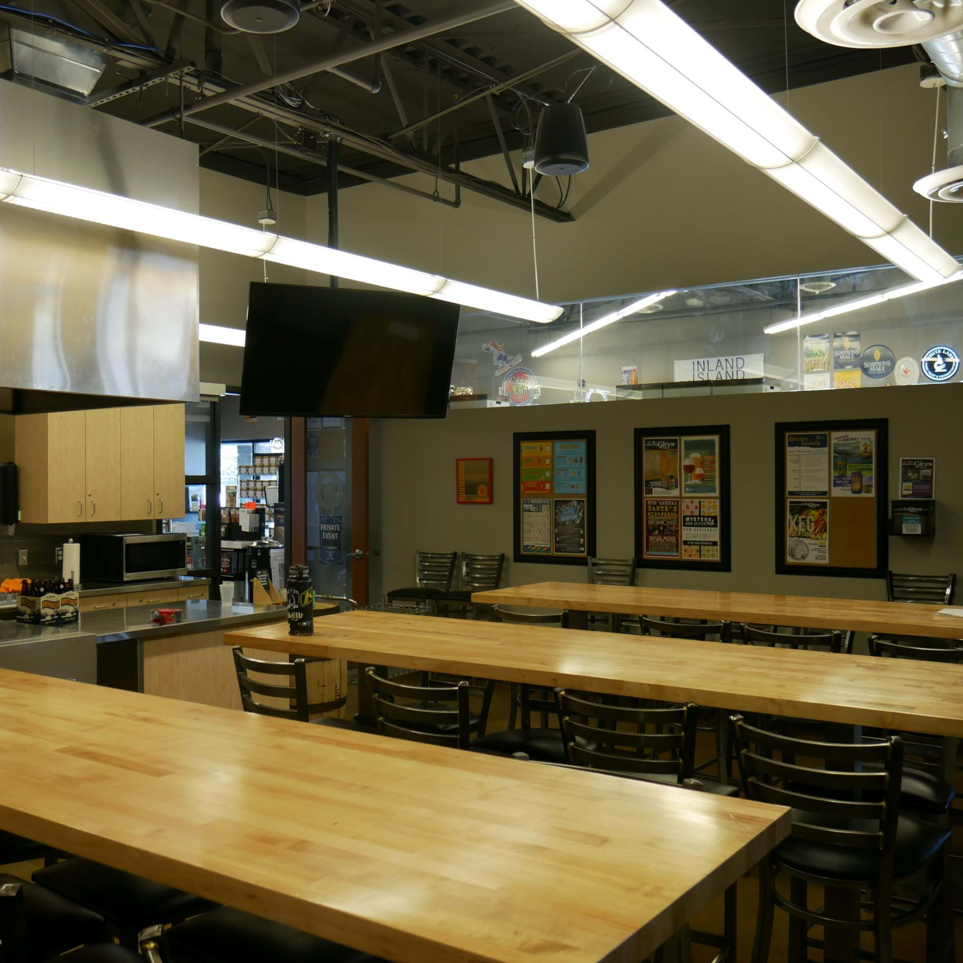 A spacious kitchen and dining area with stainless steel appliances, long wooden tables, and a large screen mounted on the wall.