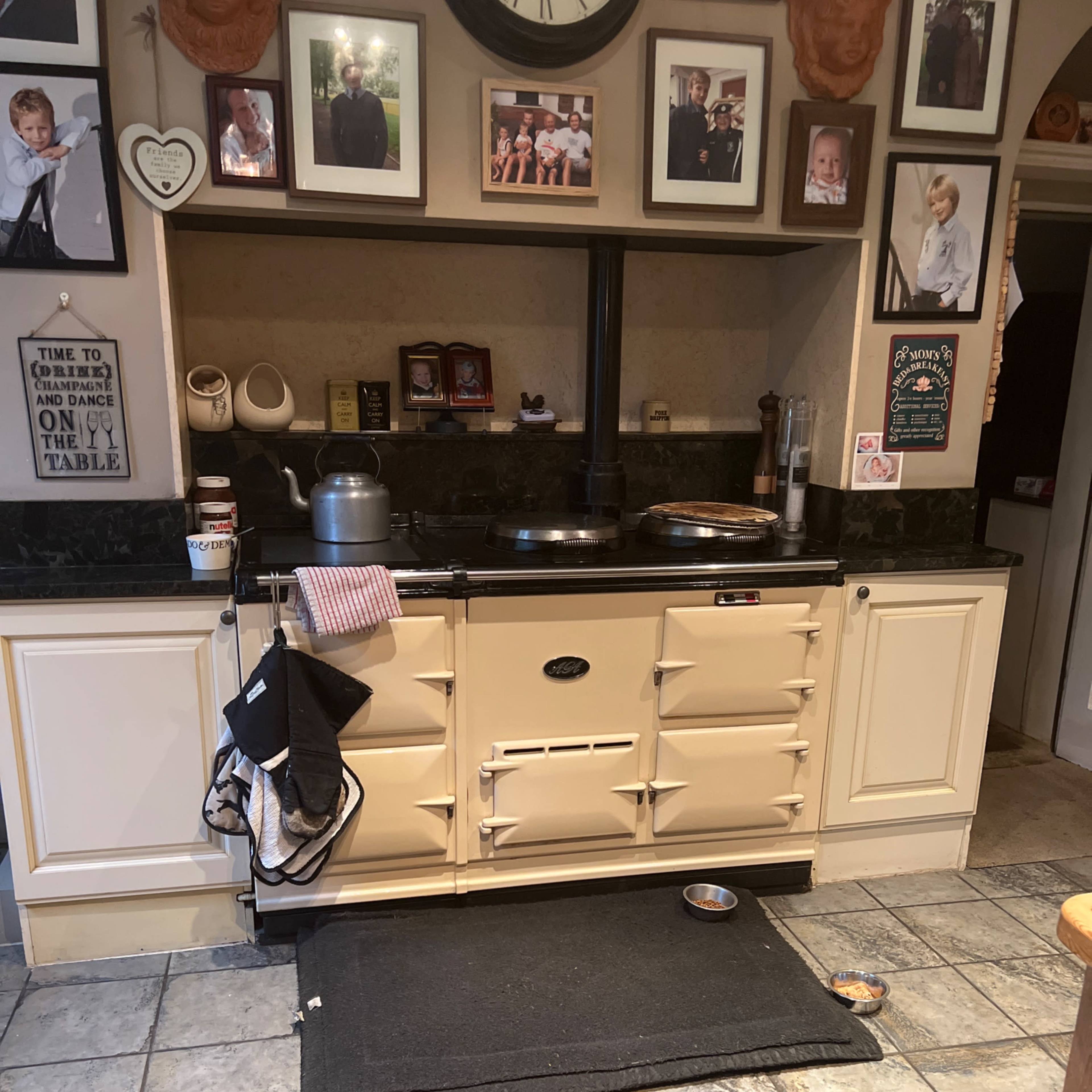 A retro-style kitchen features a large cream-colored stove, black countertops, and a collection of framed photos on the wall.