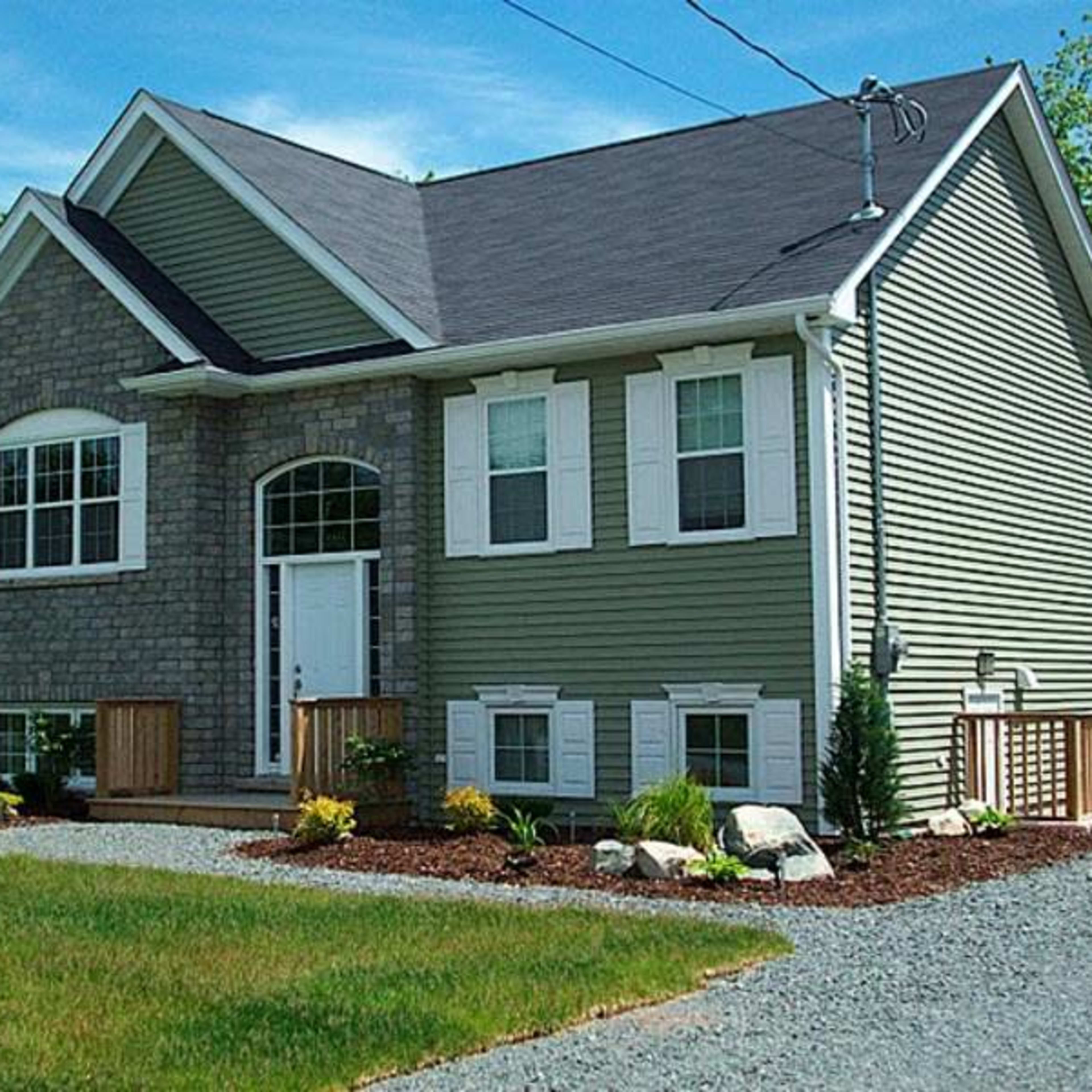 A two-story house features a stone front, gray siding, and a landscaped yard with shrubs and rocks.