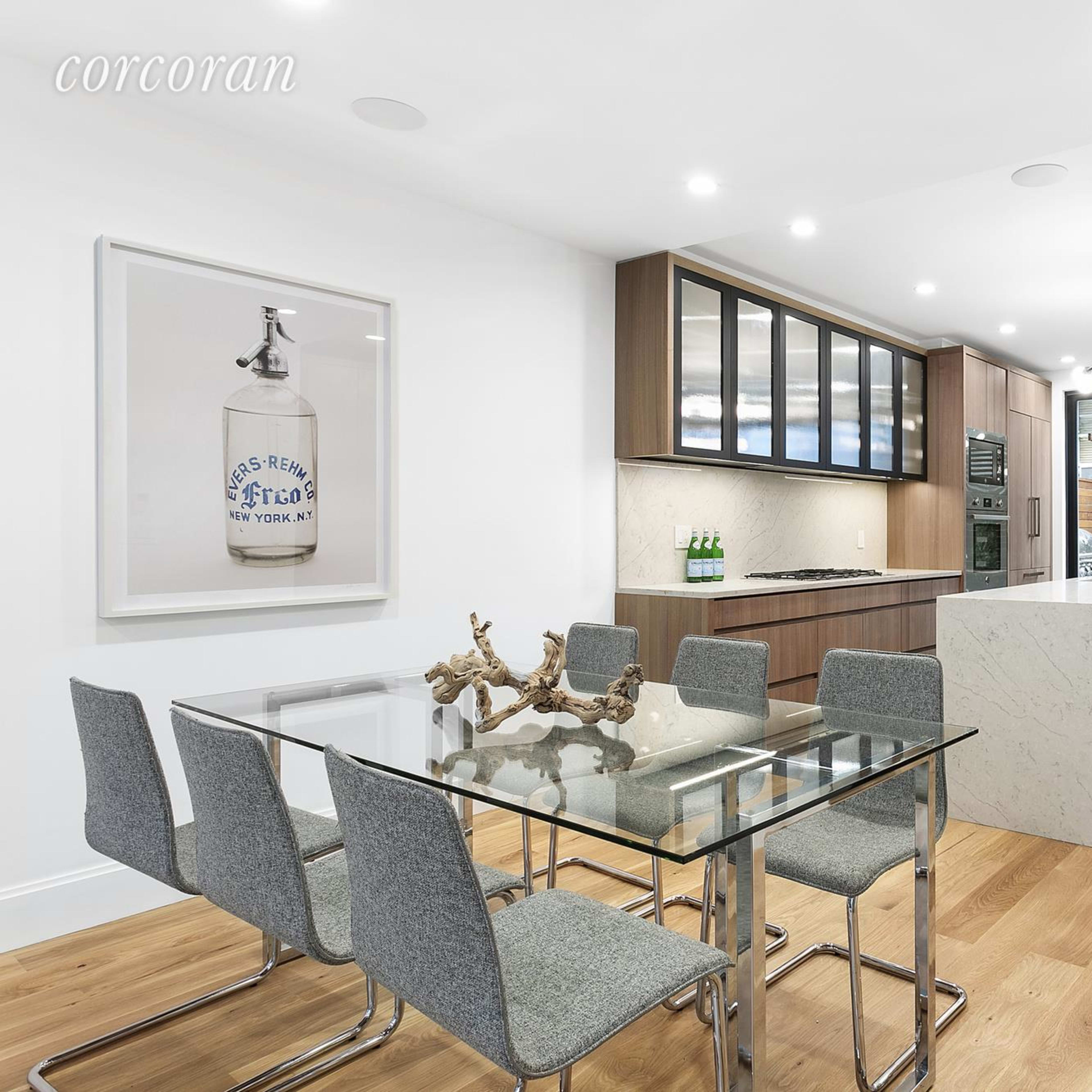 A modern kitchen and dining area featuring a glass table with six chairs, an island with a marble countertop, and large windows providing natural light.