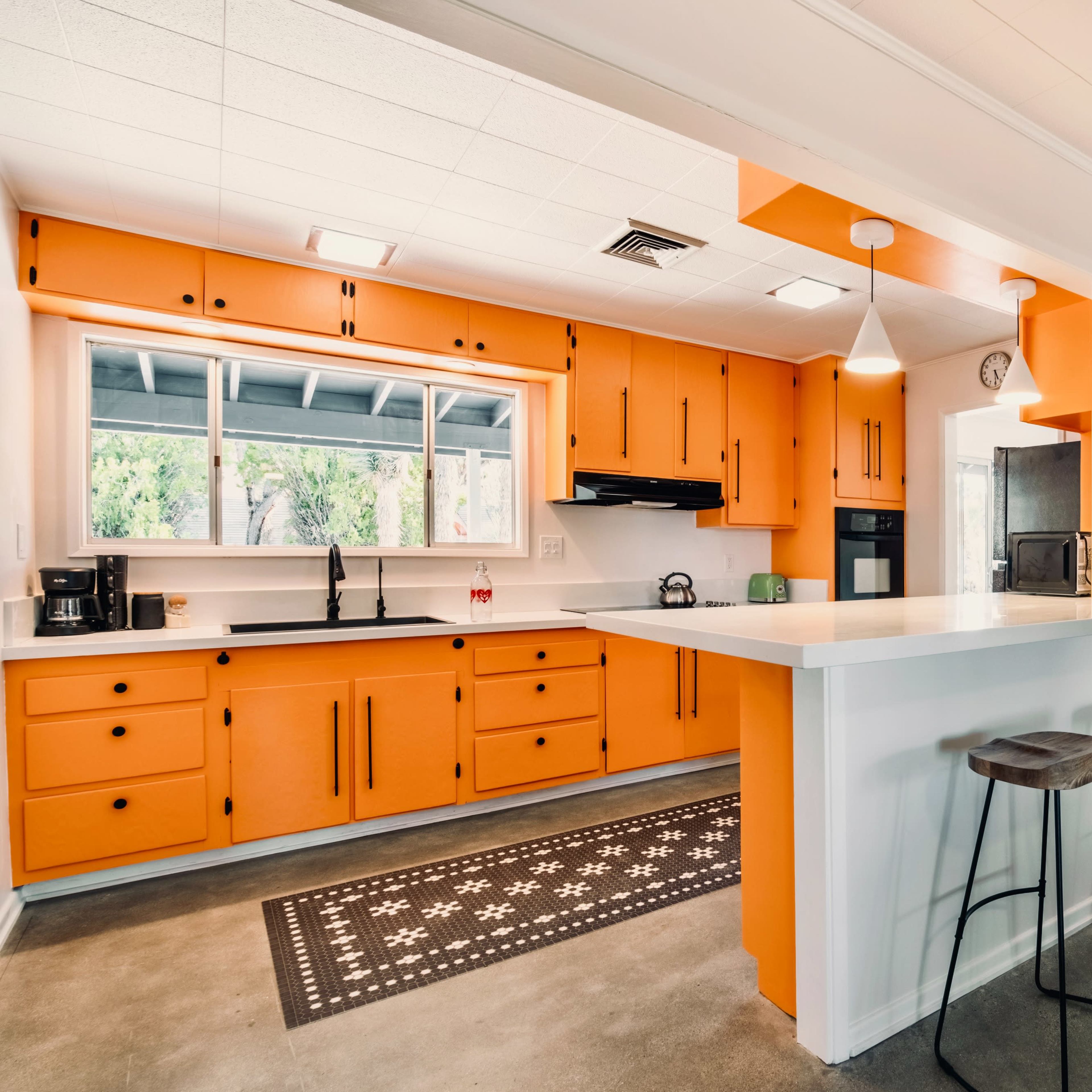 The kitchen features orange cabinets, a central island with bar stools, and a view of a dining area with a table and chairs.