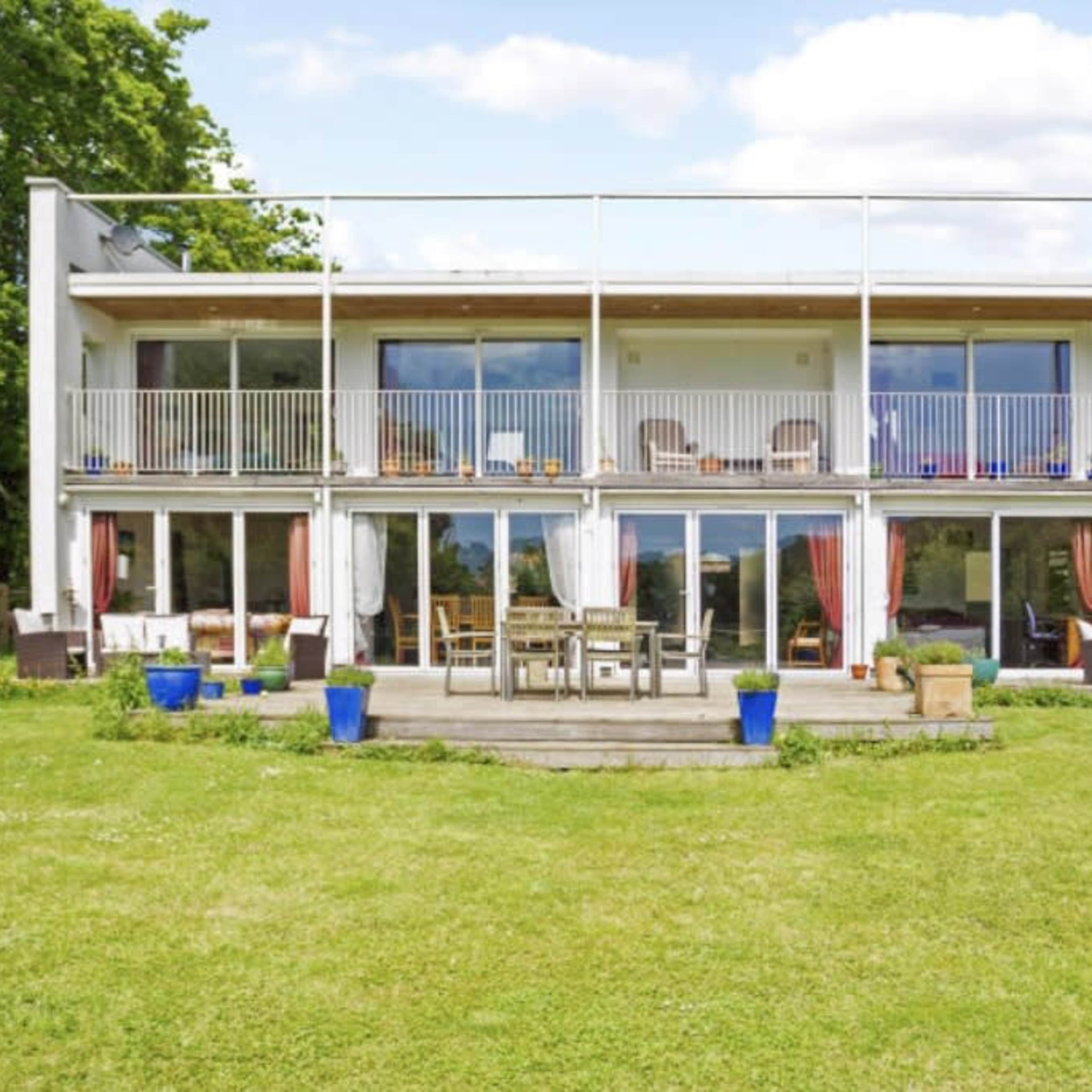 A modern two-story house with large glass doors and balconies overlooks a grassy yard.