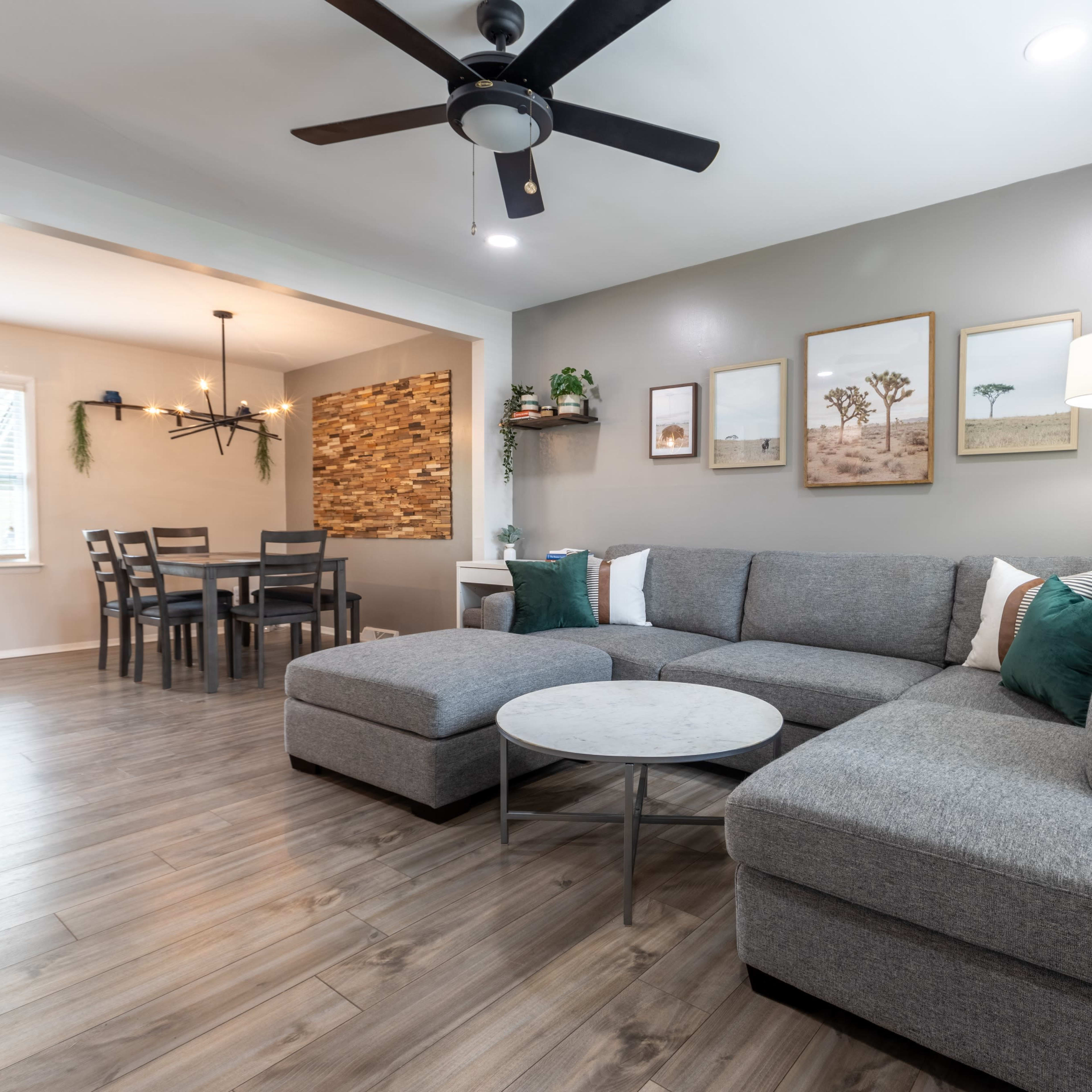 The room features a modern gray sectional sofa, a round coffee table, and a dining area with a wooden table and chairs in an open layout.