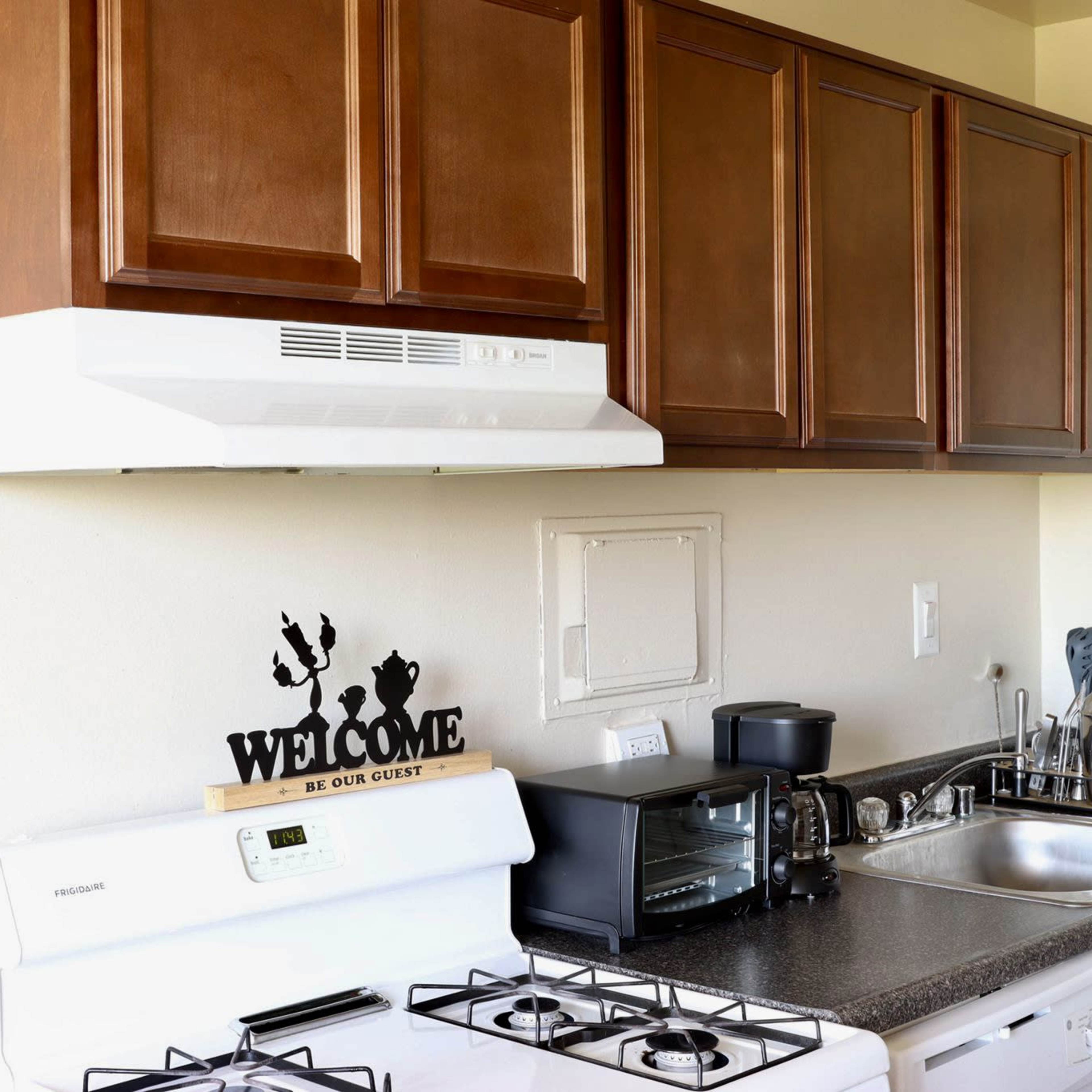 A kitchen with wooden cabinetry, a white gas stove, and various kitchen appliances on a countertop.