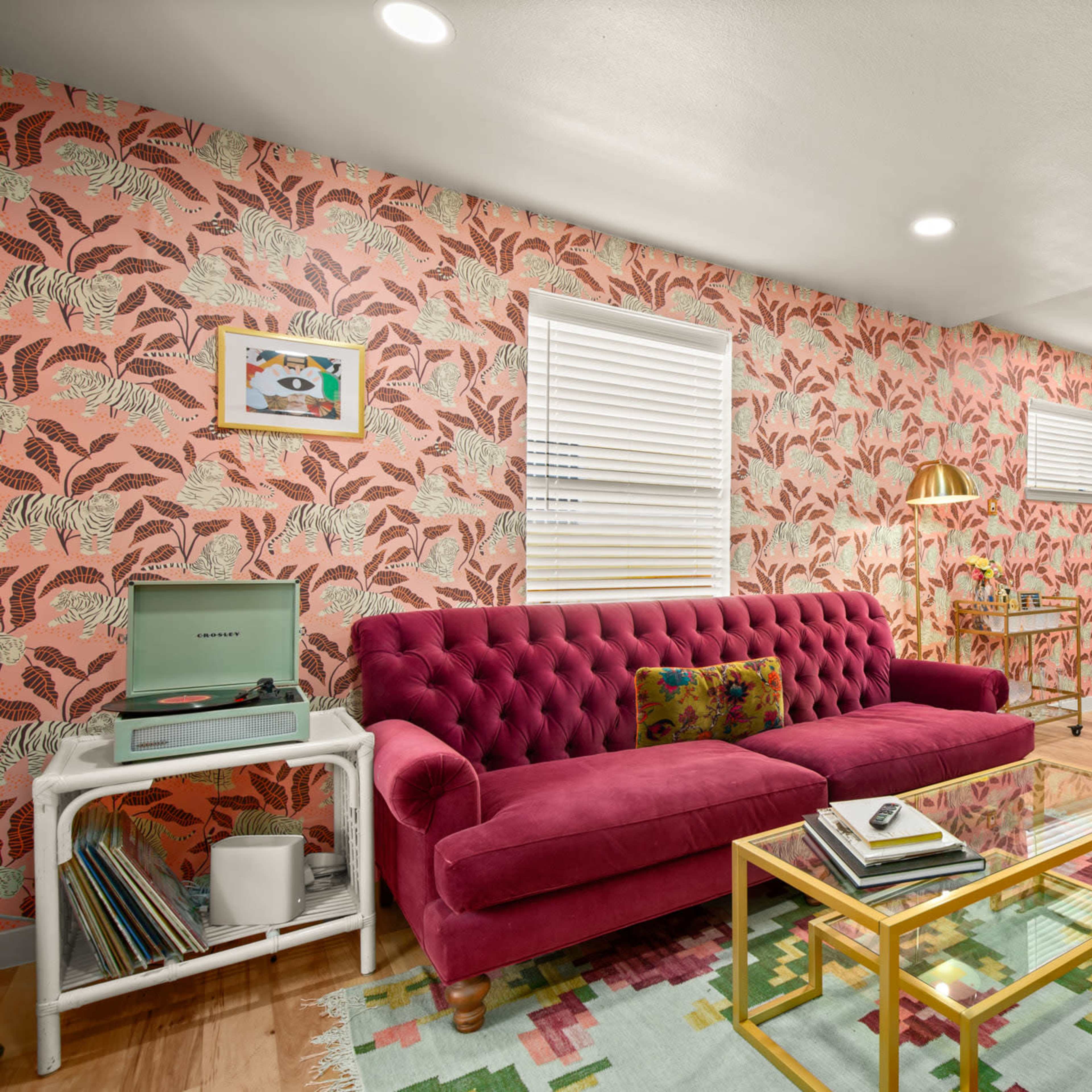 A stylish living room with a pink tufted sofa, patterned wallpaper, a coffee table, and a dining area with a round table and chairs.