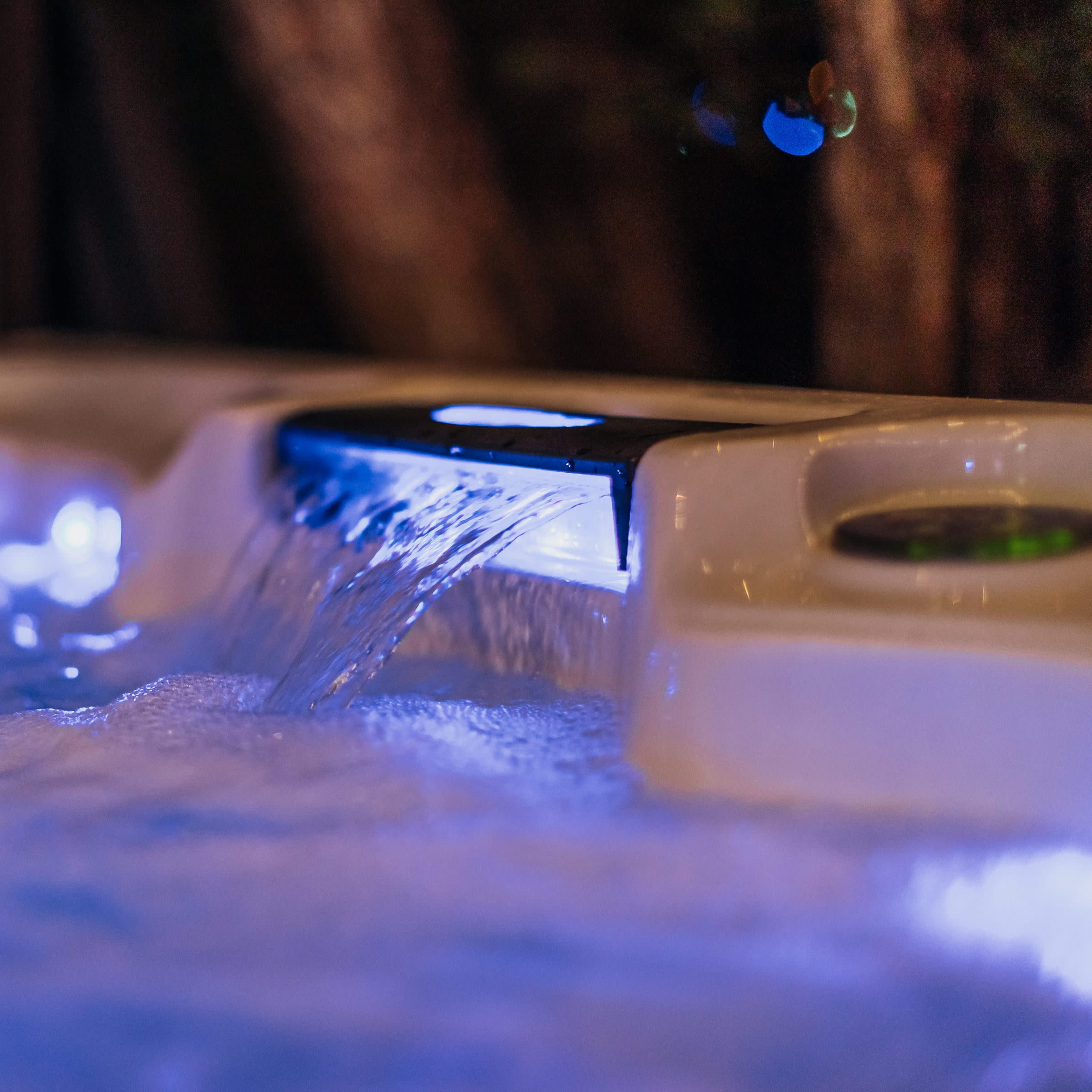 A hot tub with glowing blue lights and flowing water is seen in a dimly lit outdoor setting.