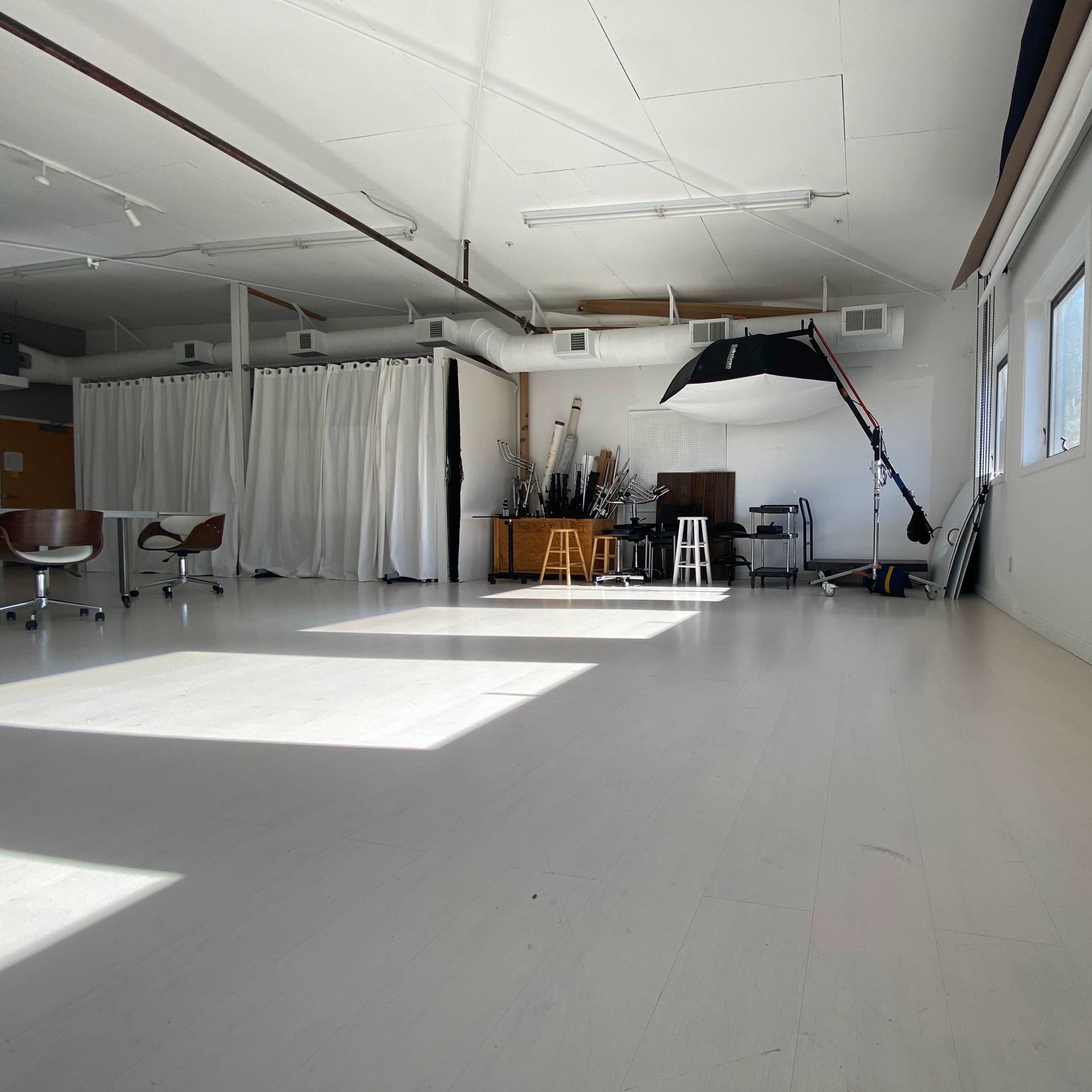 A bright, spacious studio with white walls, wooden furniture, and a large softbox light on a stand.