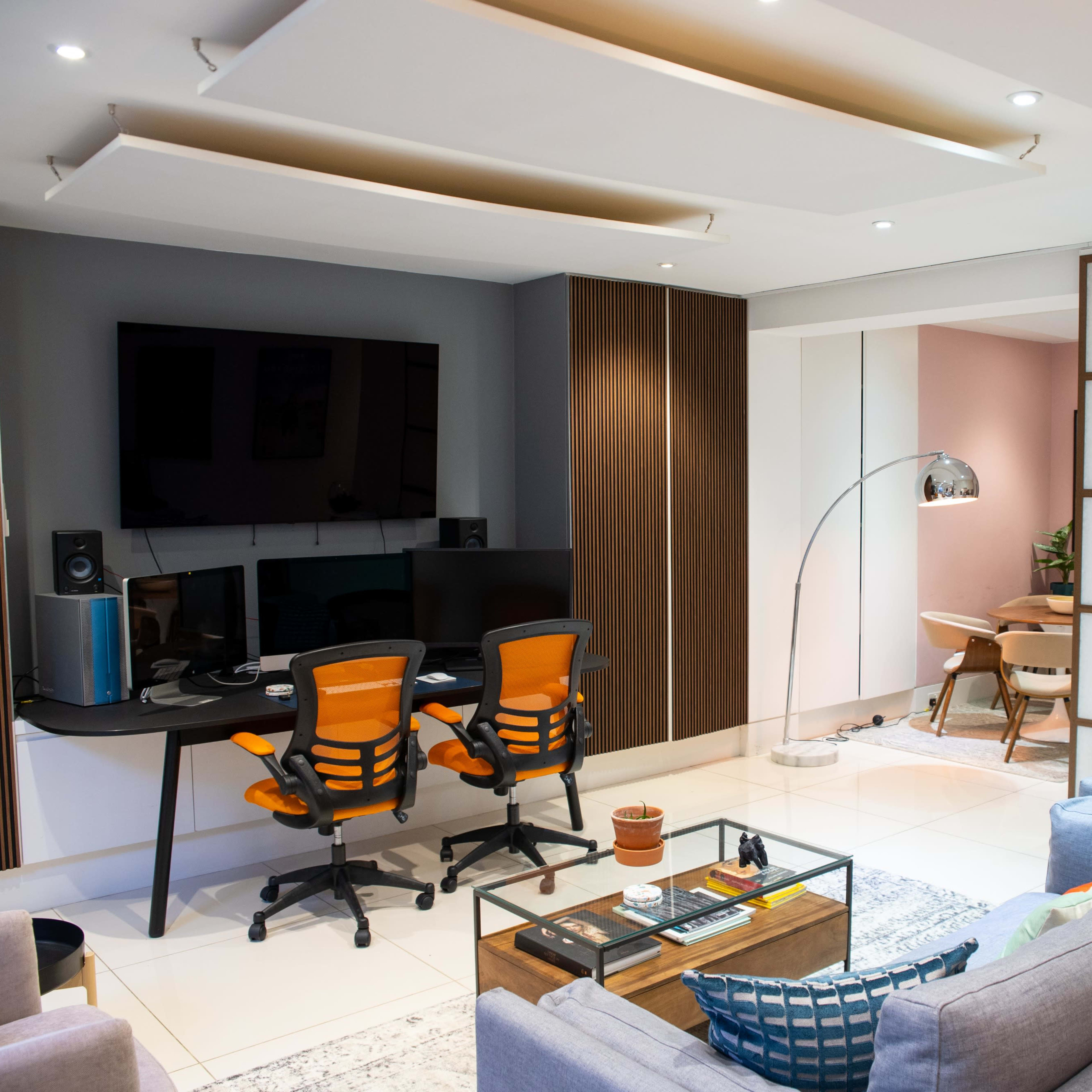 A modern living room with a seating area, a desk with two chairs, and an adjacent dining space.