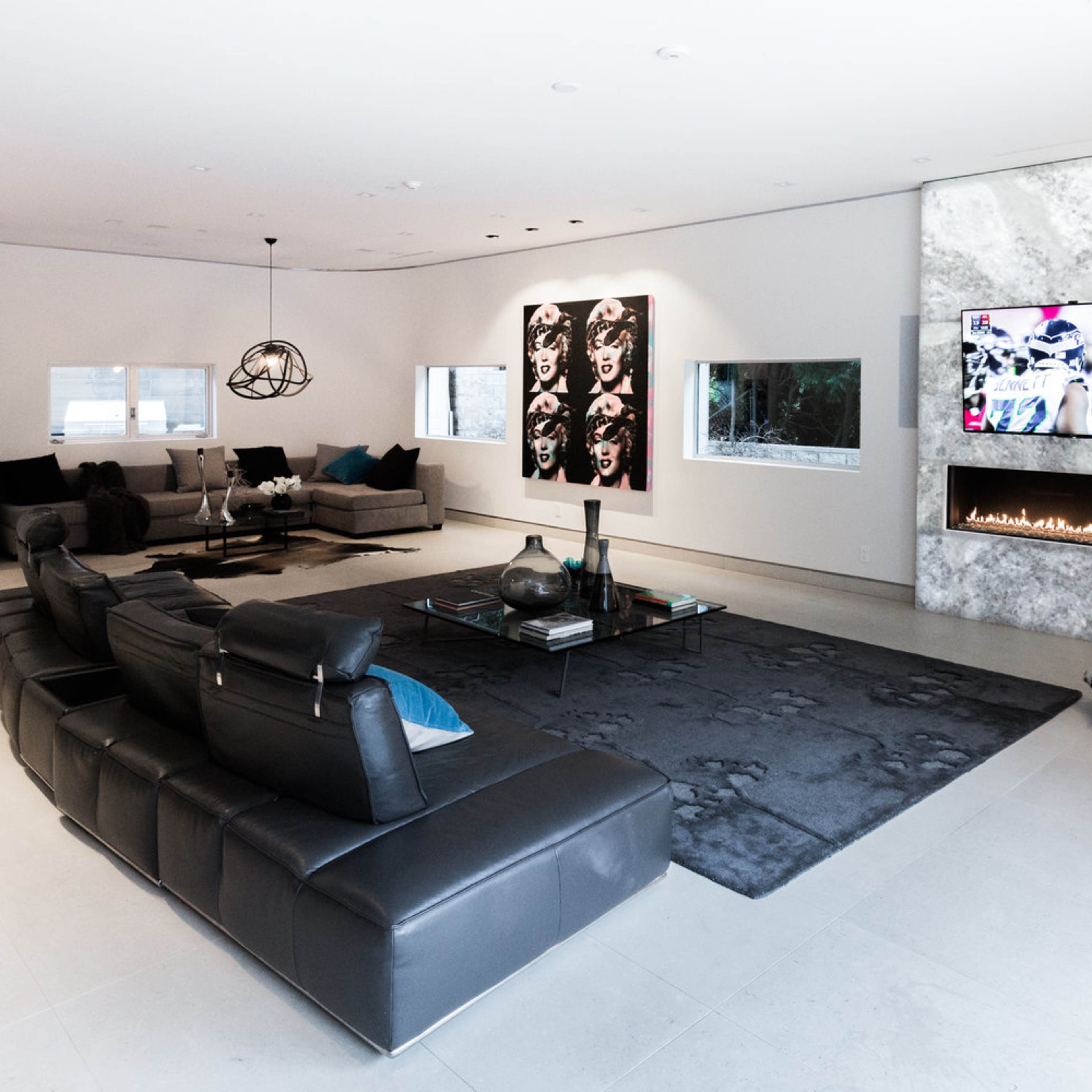 A modern living room features a sleek black sectional sofa, a flat-screen TV mounted on a stone wall, and two large artworks.