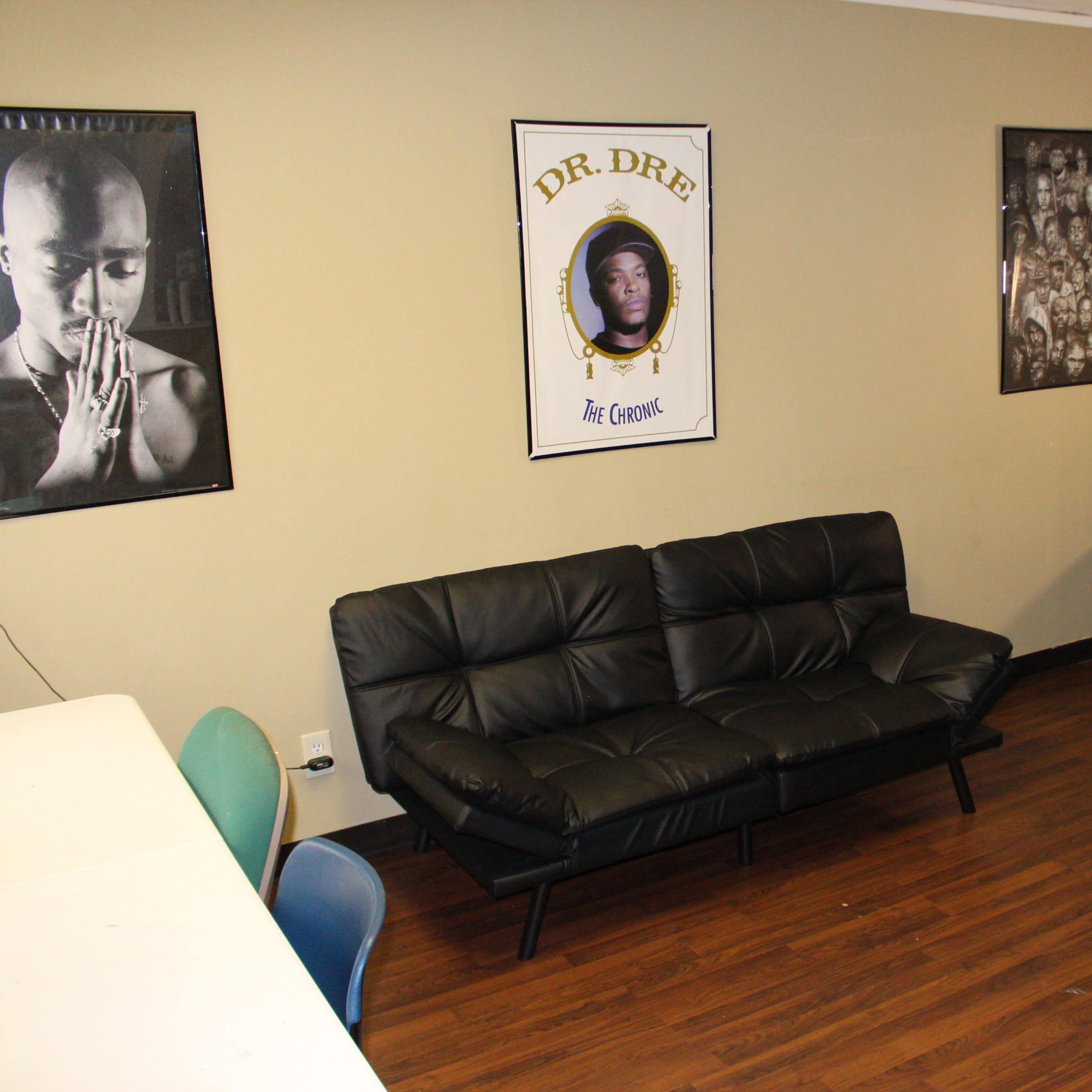 A room with a black leather sofa, two armchairs, a table, and several framed portraits on the walls.