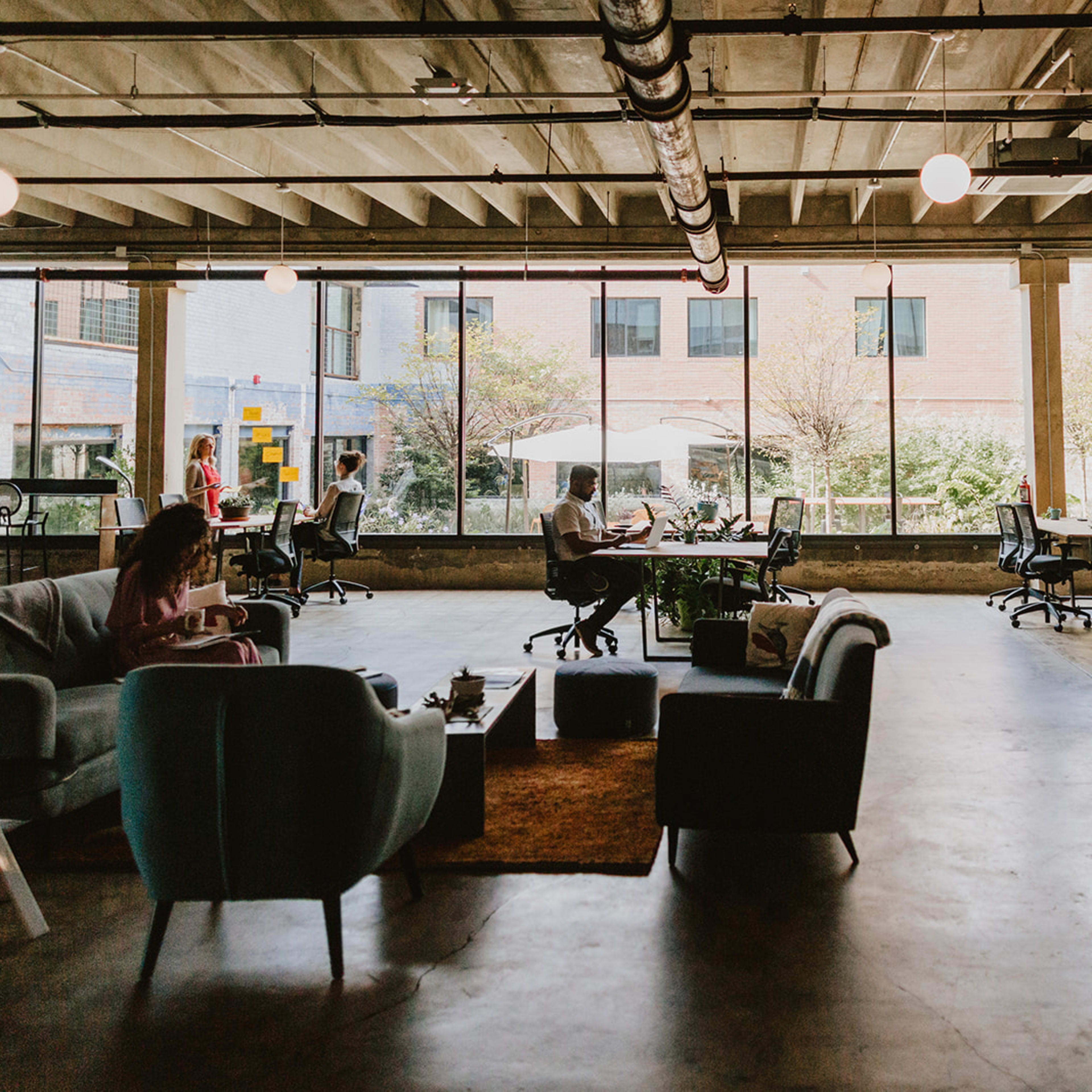 A modern office space features several workstations and comfortable seating areas, with large windows allowing natural light to fill the room.