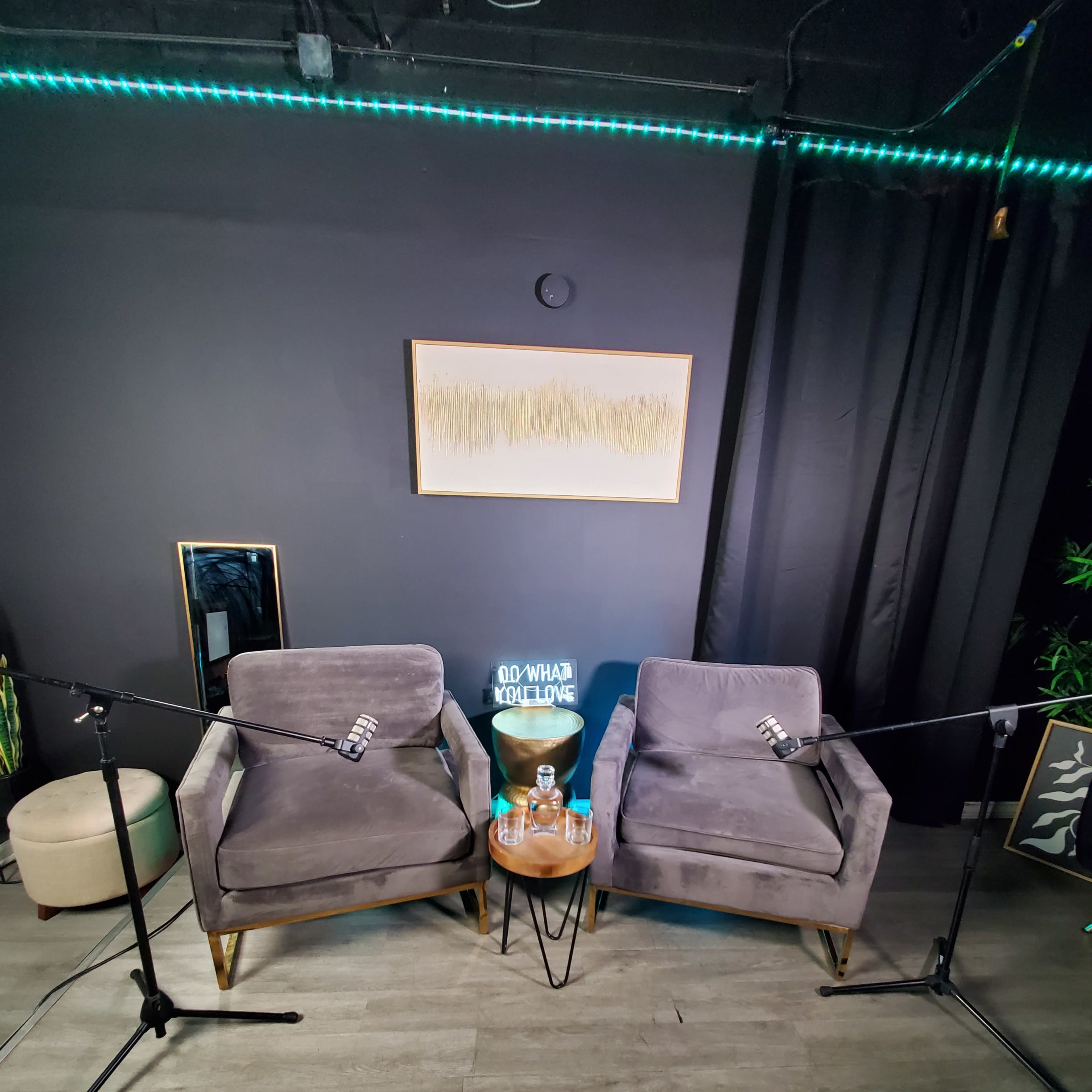 Two gray chairs positioned opposite each other with microphones on stands and a small table between them, set in a room with dark walls and soft lighting.