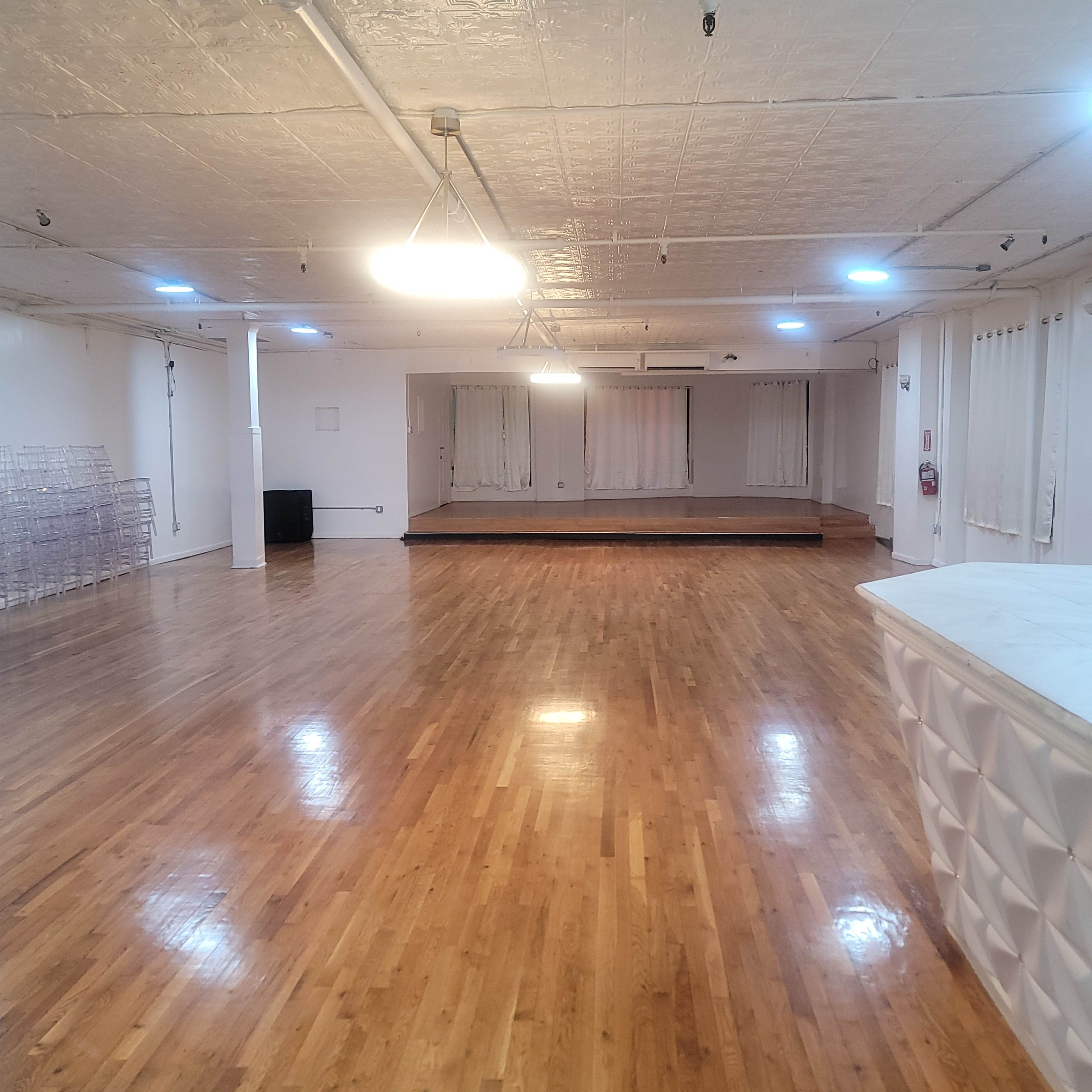 A spacious room with hardwood flooring, bright overhead lighting, and a raised platform at one end.