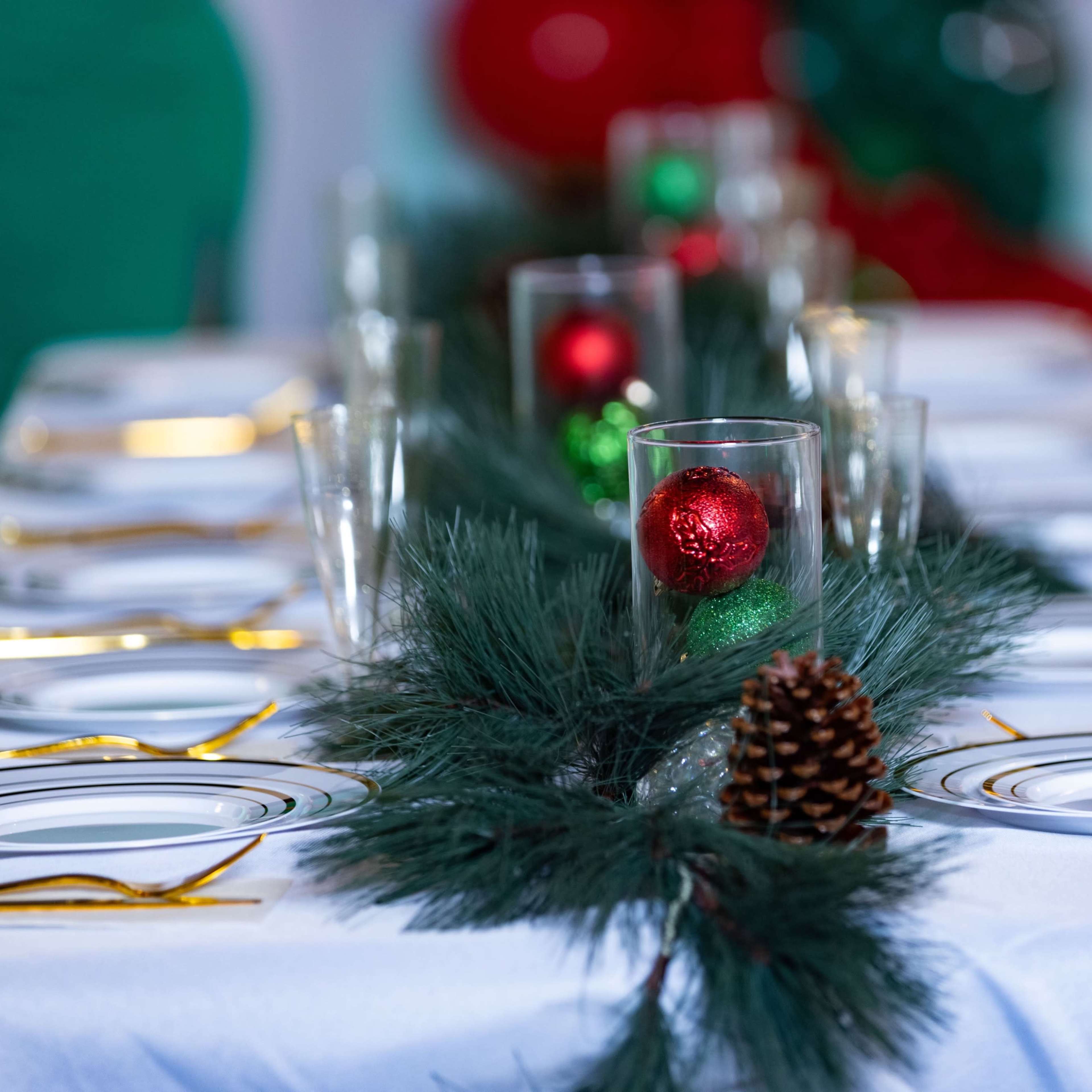 A festive dining table is set with plates and glasses, adorned with greenery and decorative ornaments.