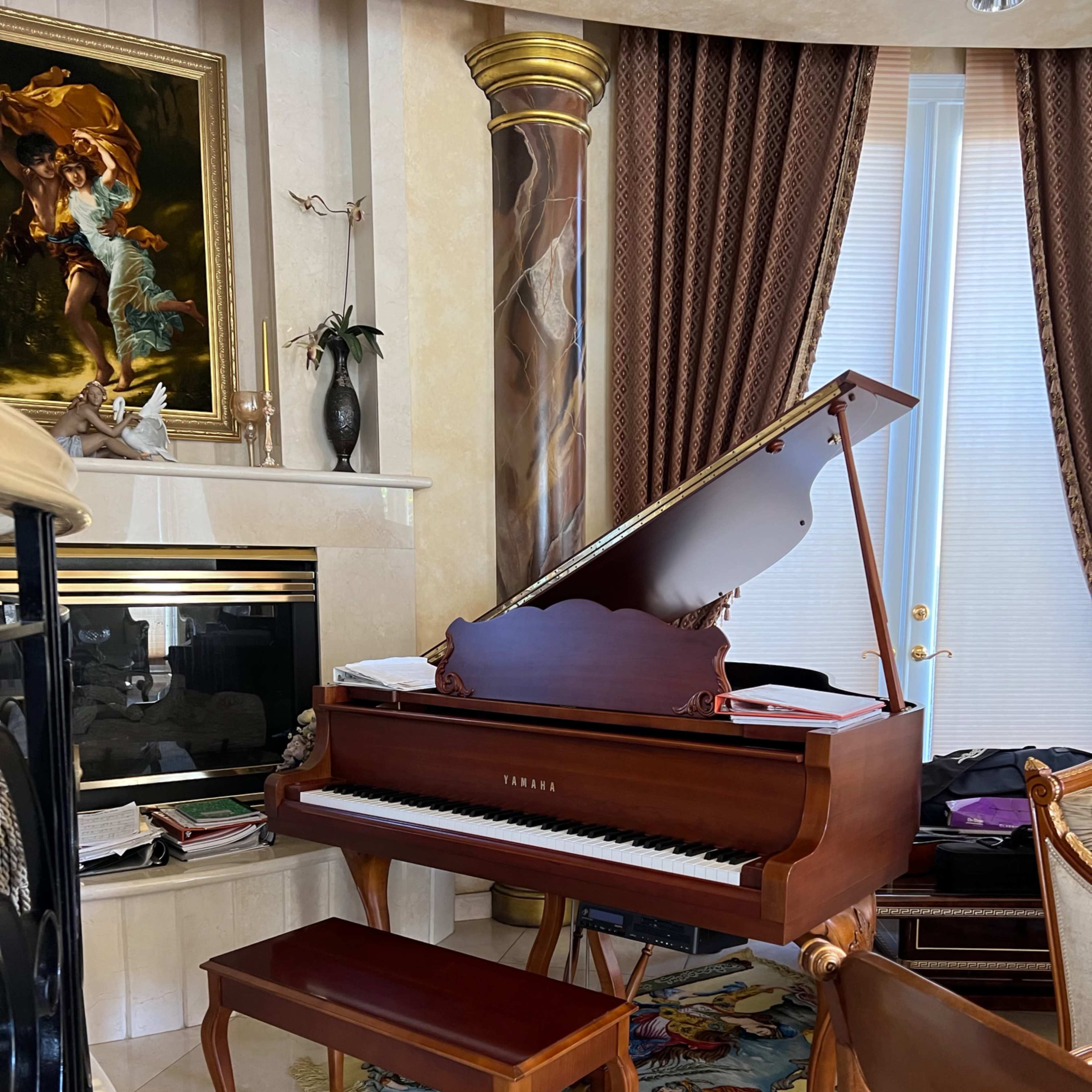 A grand piano with a matching bench sits beside a fireplace in a room adorned with ornate decor and furnishings.
