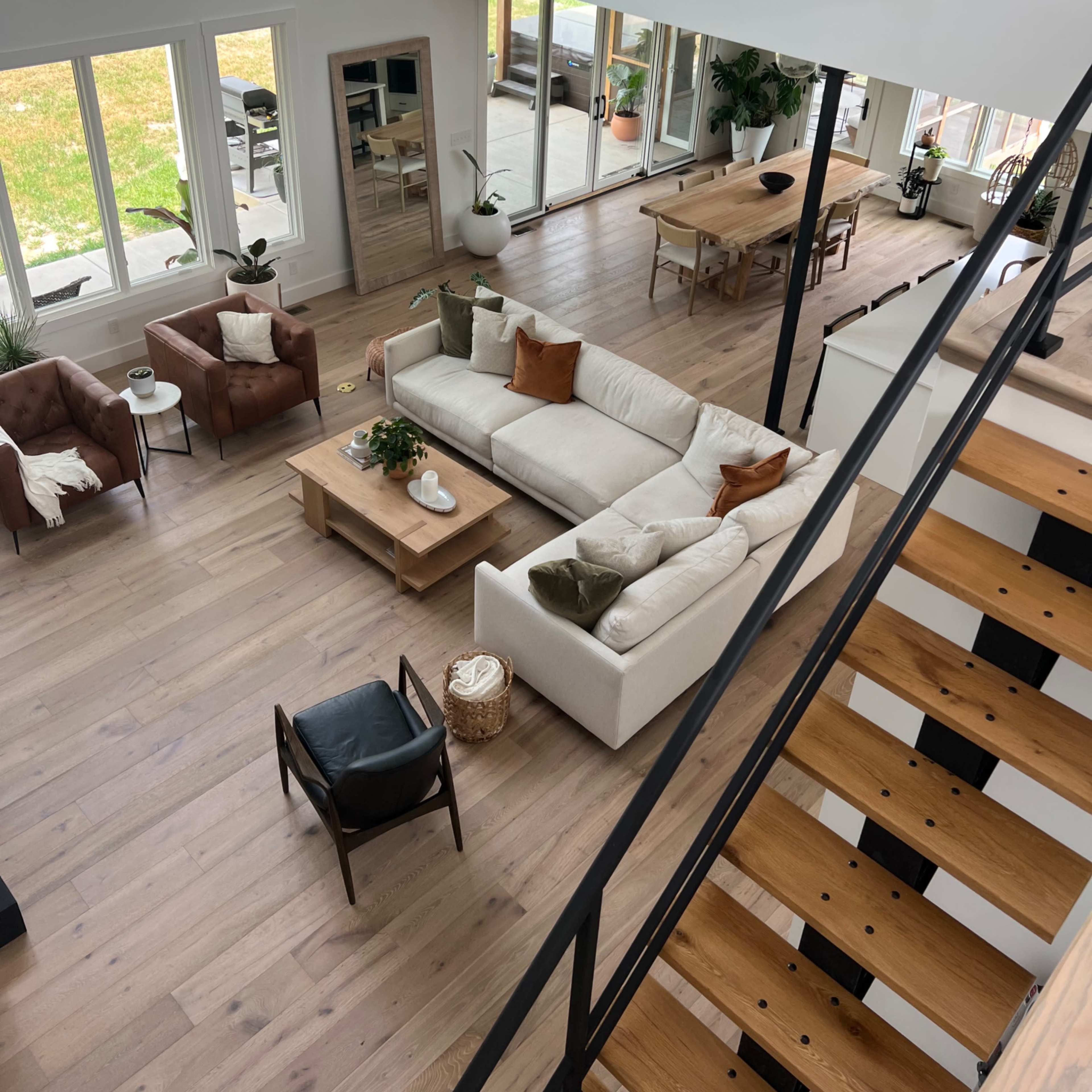 A spacious living area features a sectional sofa, wooden furniture, and large windows overlooking a yard.