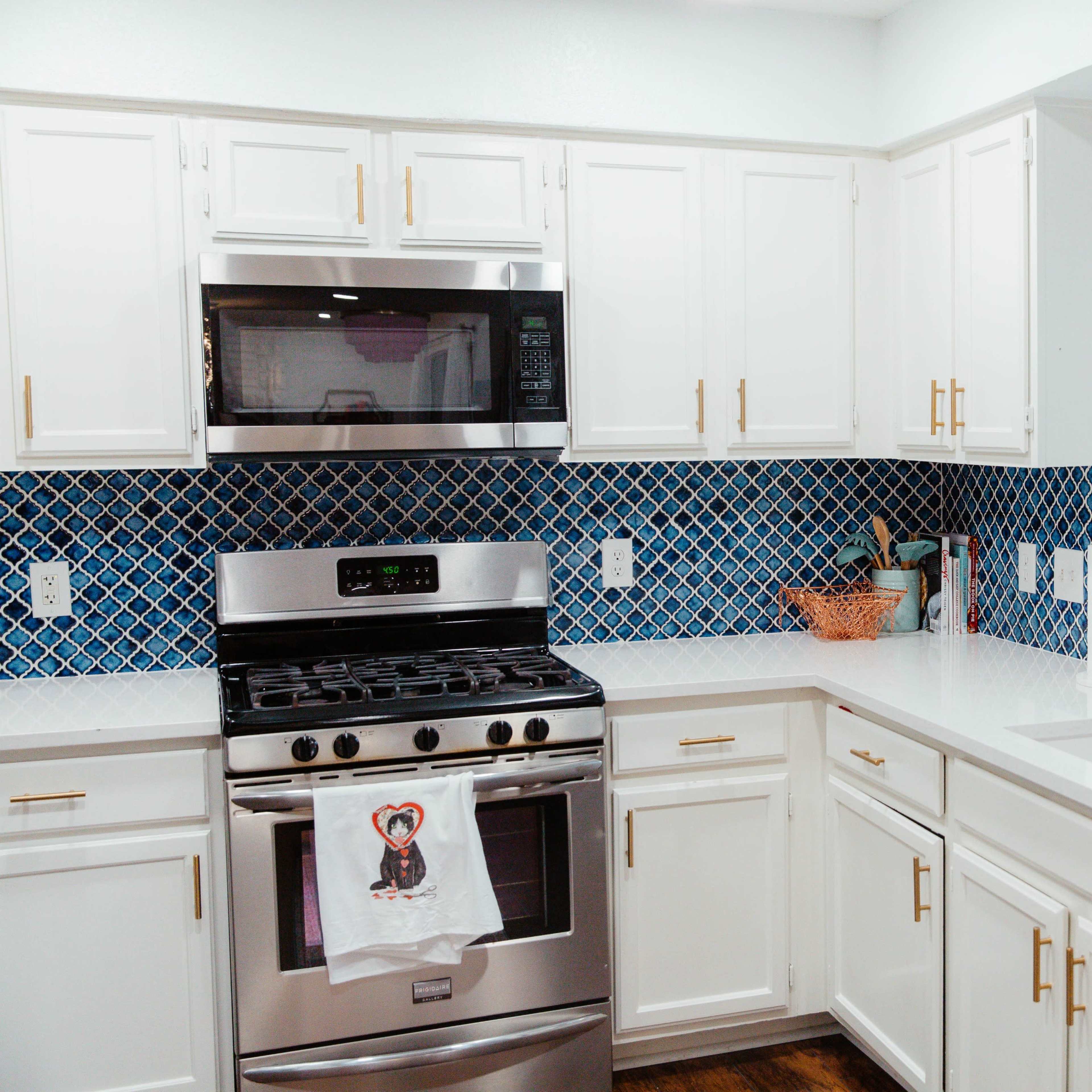 A modern kitchen features white cabinetry, a stainless steel gas stove, and blue tiled backsplash.