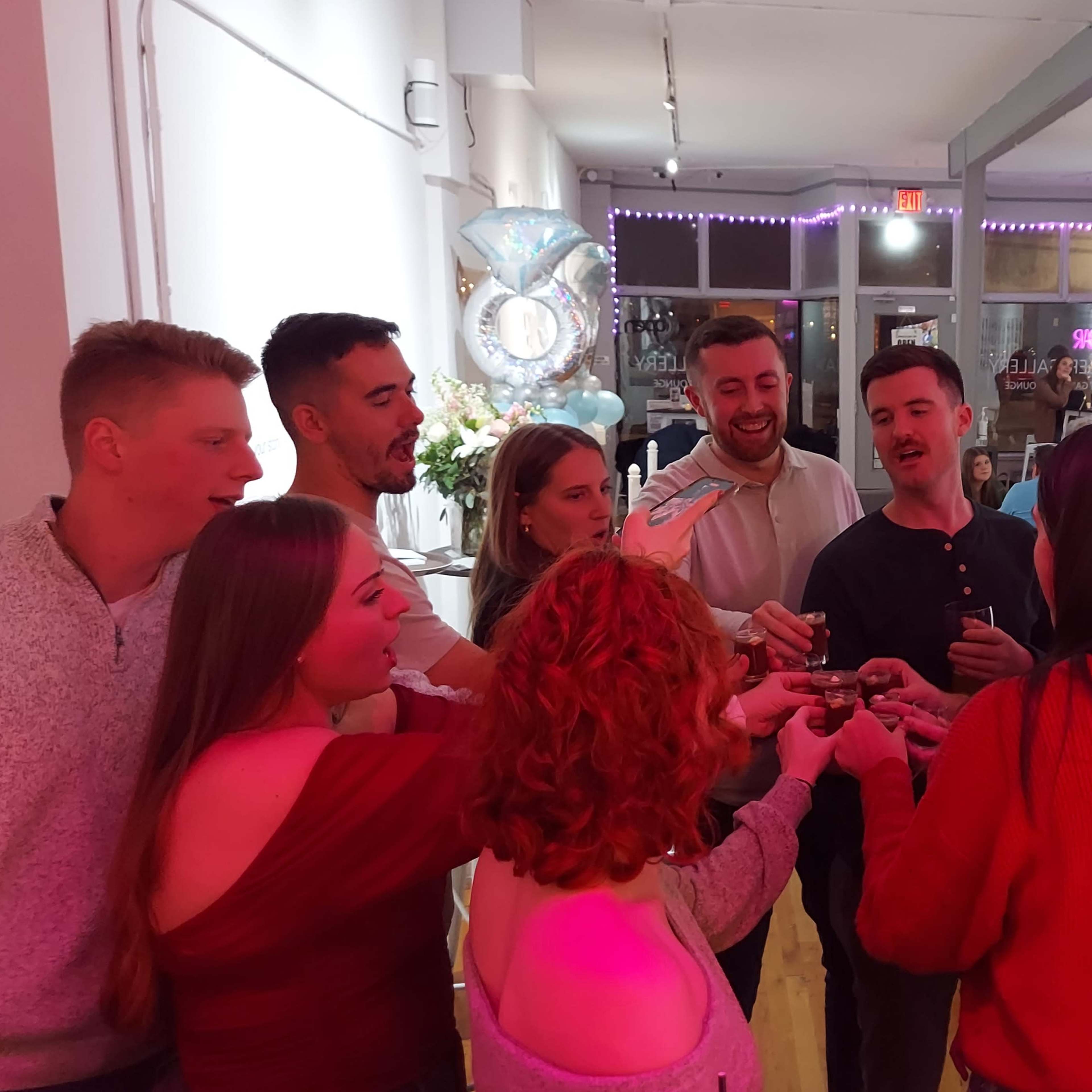 A group of people gathers around a table to toast with drinks in a brightly lit, modern interior.