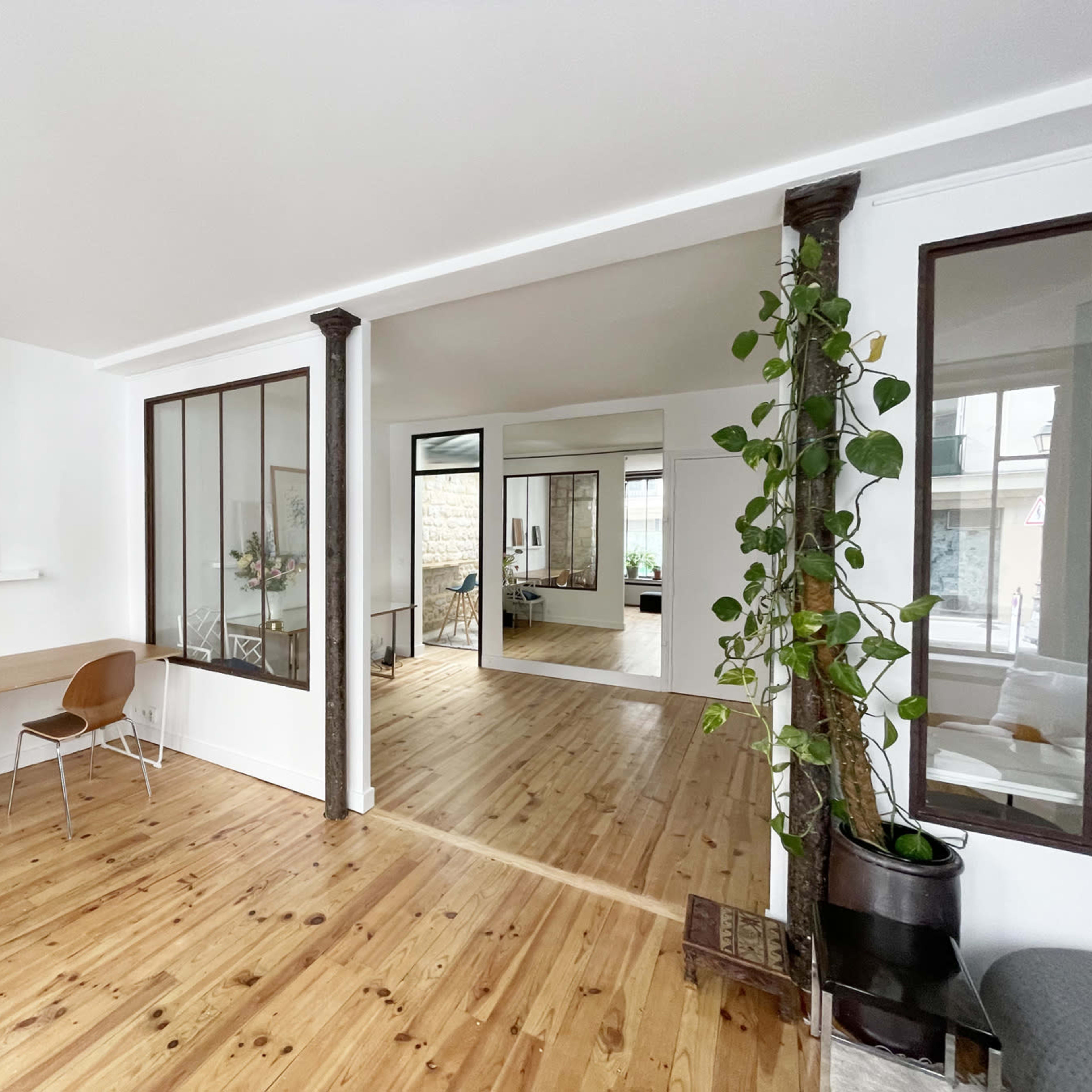 A modern, open-concept interior with wooden floors, a small workspace area with two chairs, and a glass partition leading to another room.