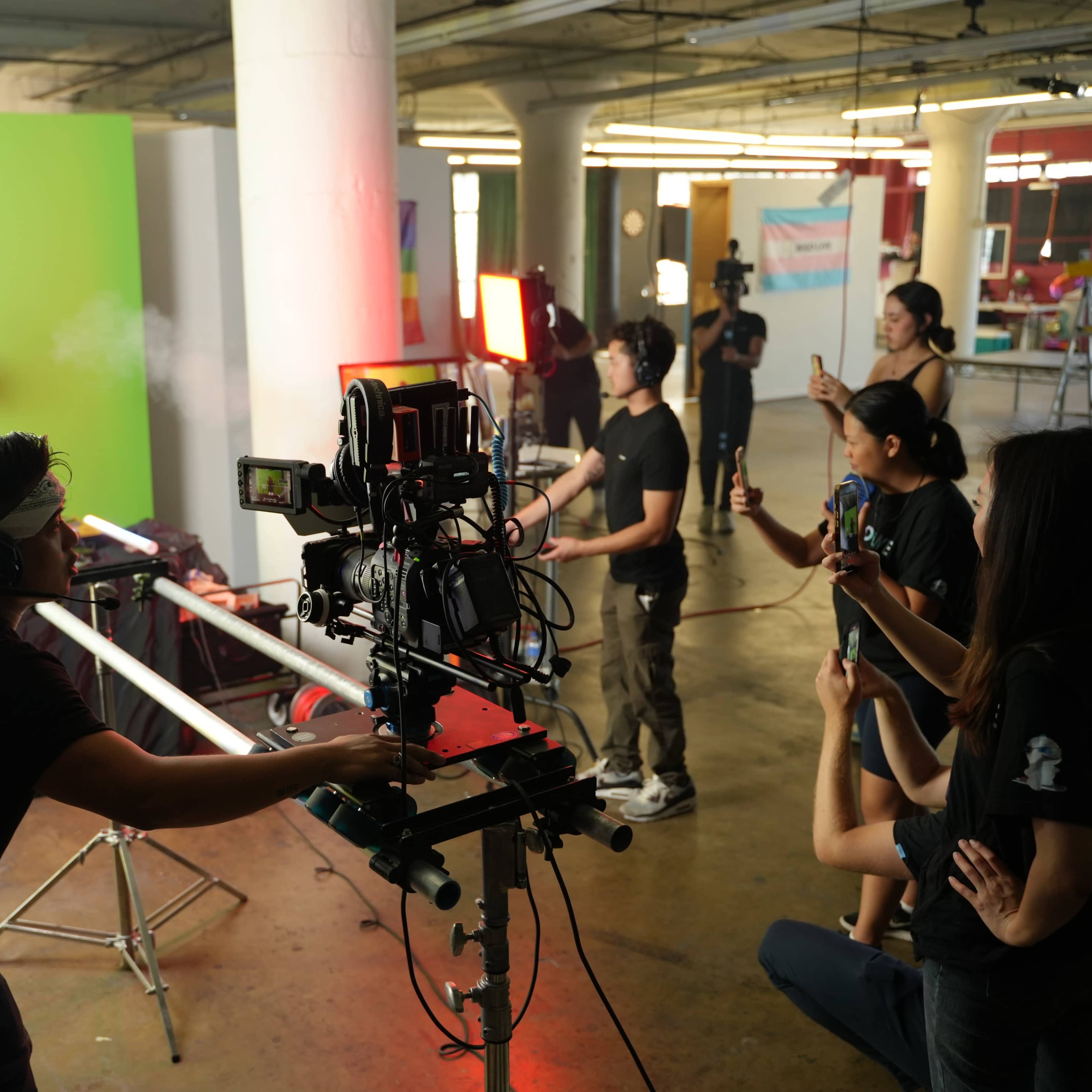 A filmmaking crew operates cameras and lighting equipment in a studio with a green screen backdrop.