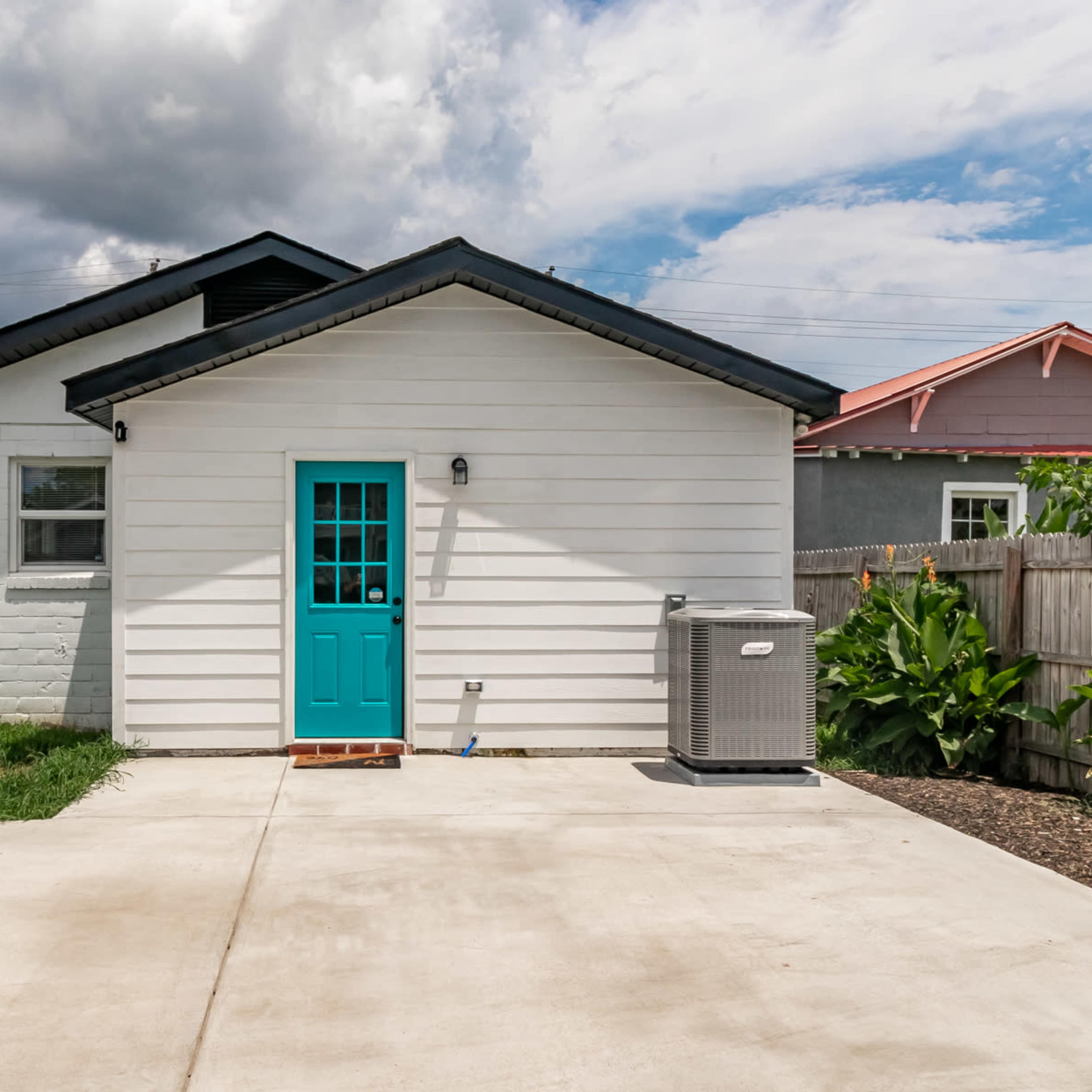 A white house with a turquoise front door and an air conditioning unit, set against a cloudy sky.