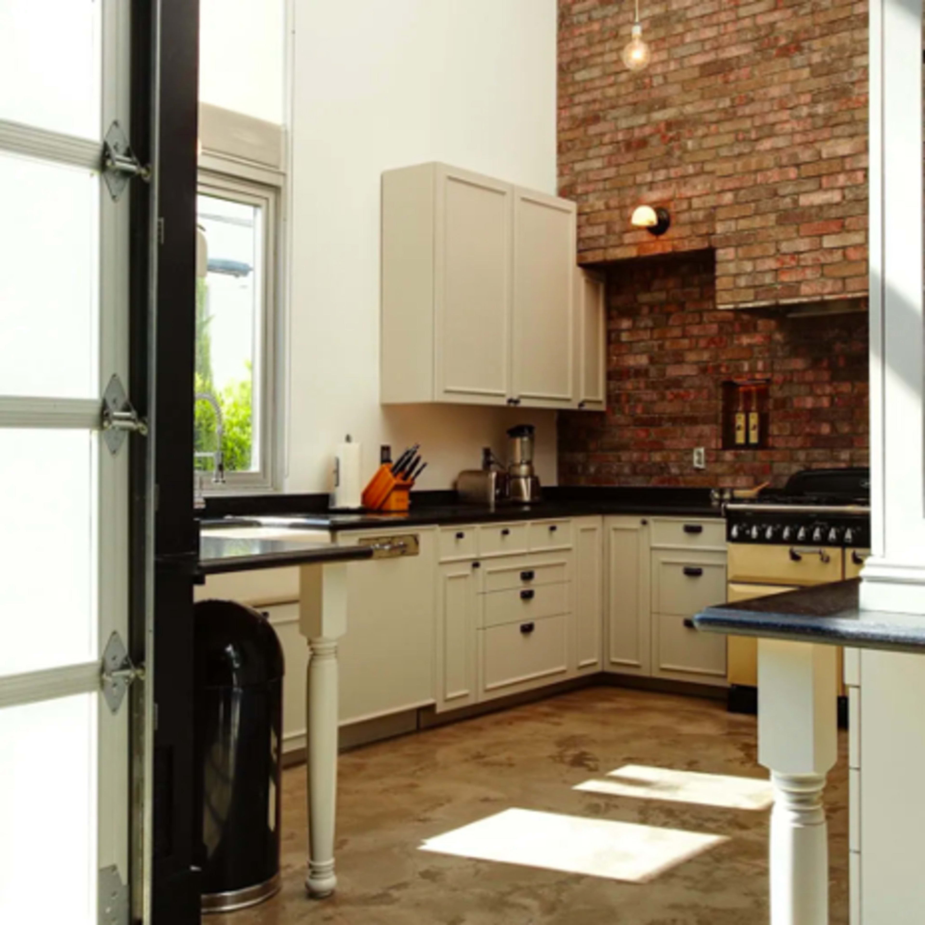 A modern kitchen with a brick wall and a mix of white cabinetry and a black countertop.
