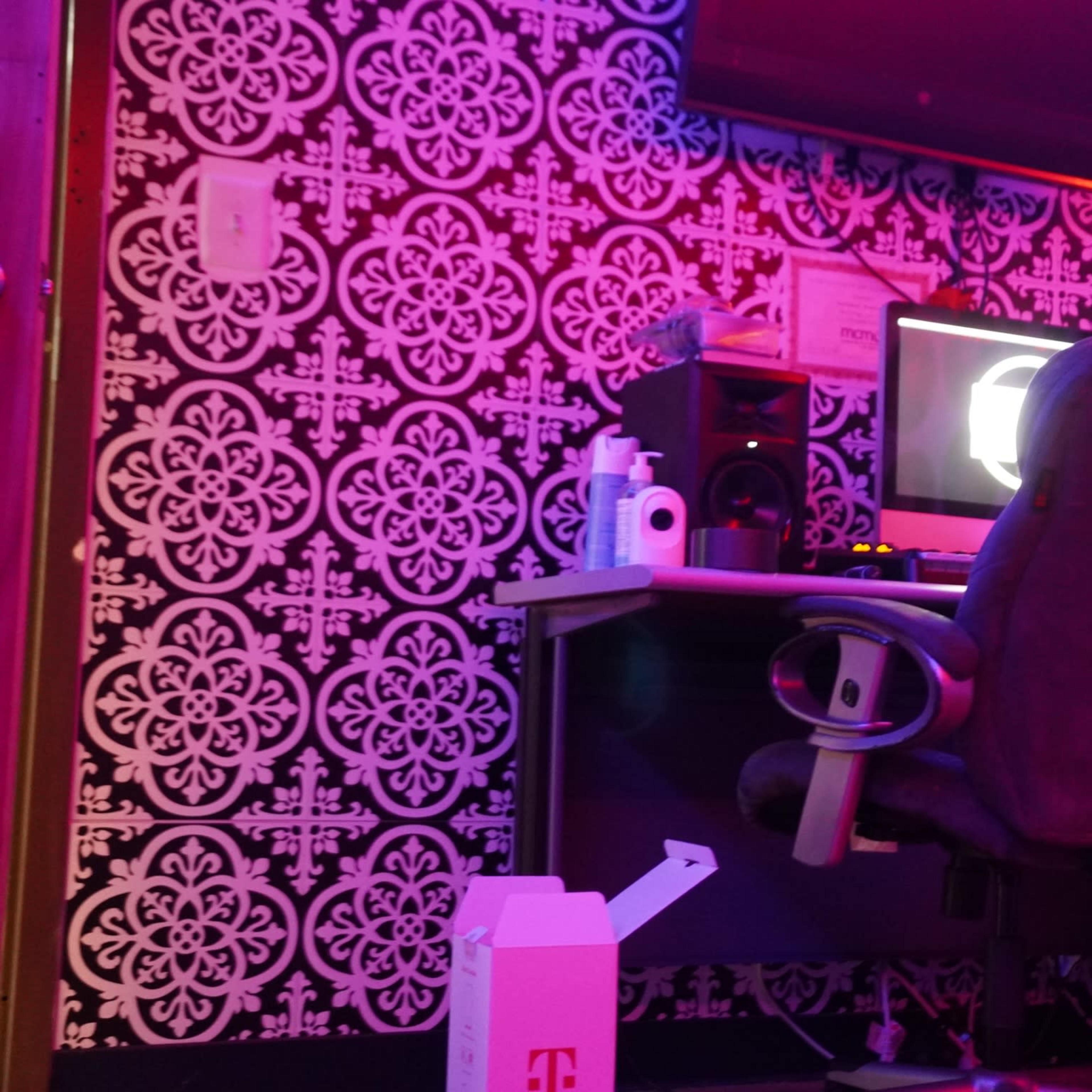 A workspace set against a patterned wall, with a computer desk featuring a monitor, speakers, and an office chair.
