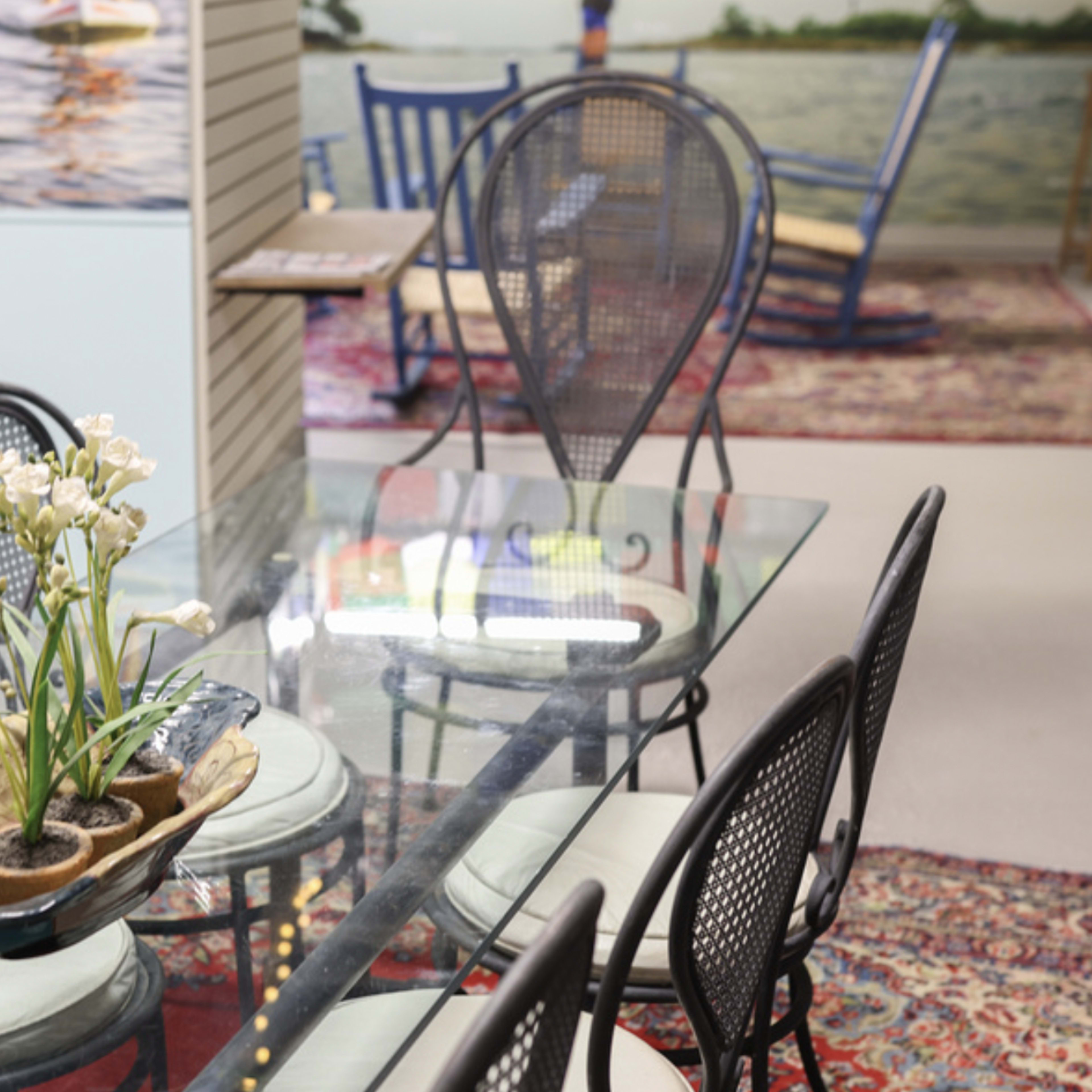 A glass dining table with a floral centerpiece is surrounded by black chairs in a brightly lit room decorated with artwork and rugs.