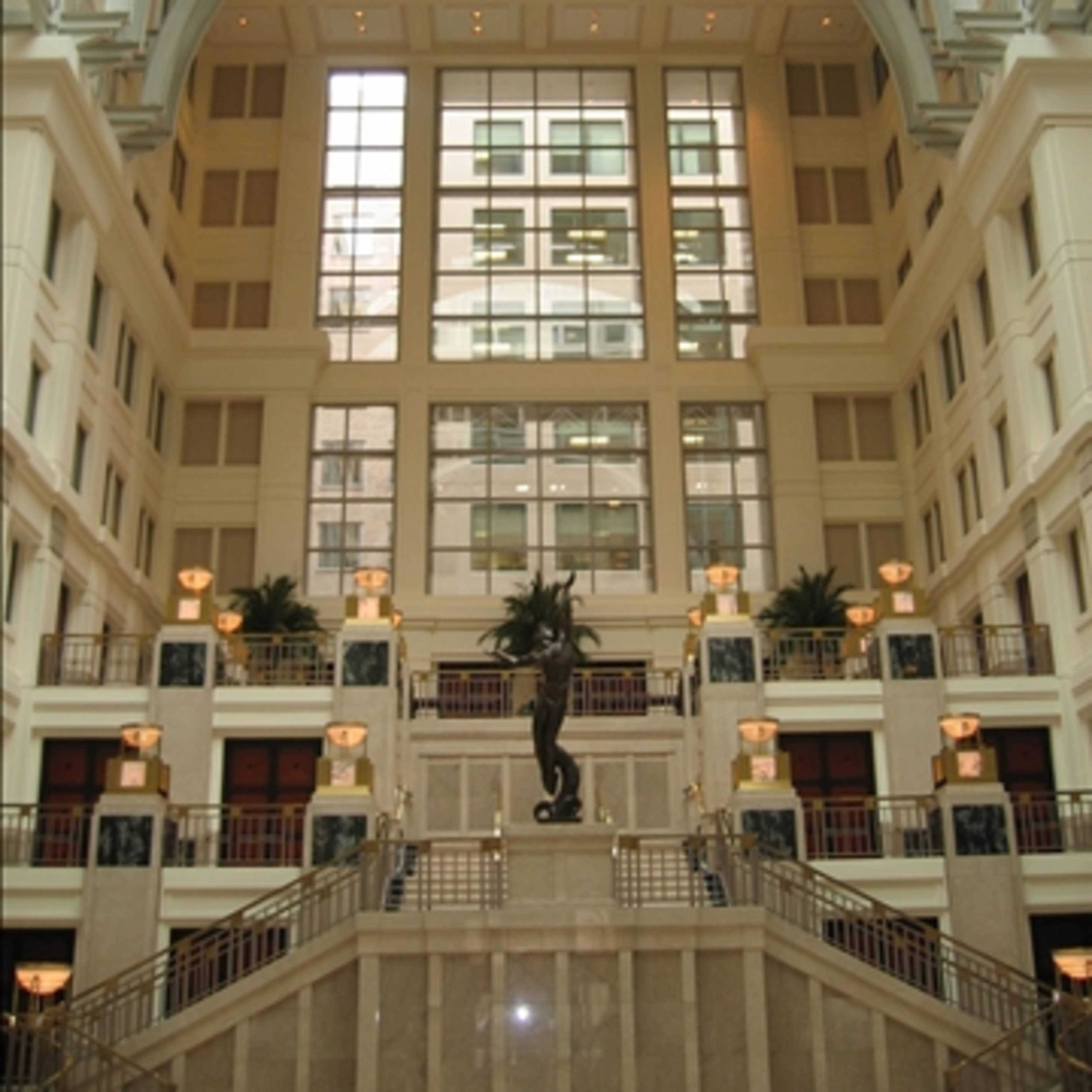A grand interior of a building featuring a large archway, a central staircase, and decorative plant elements.
