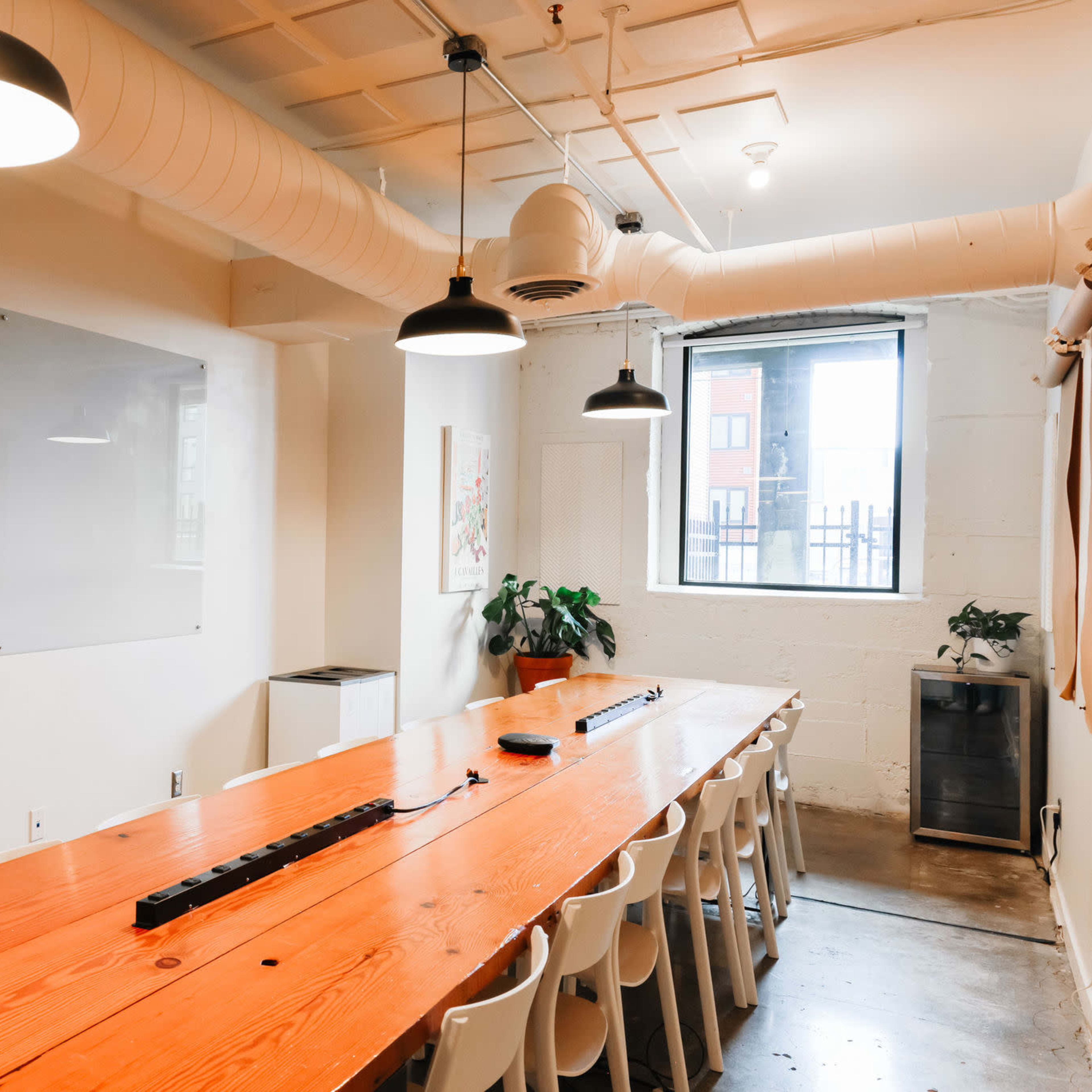 A large conference room features a long wooden table surrounded by white chairs, with a whiteboard and a window on one side.