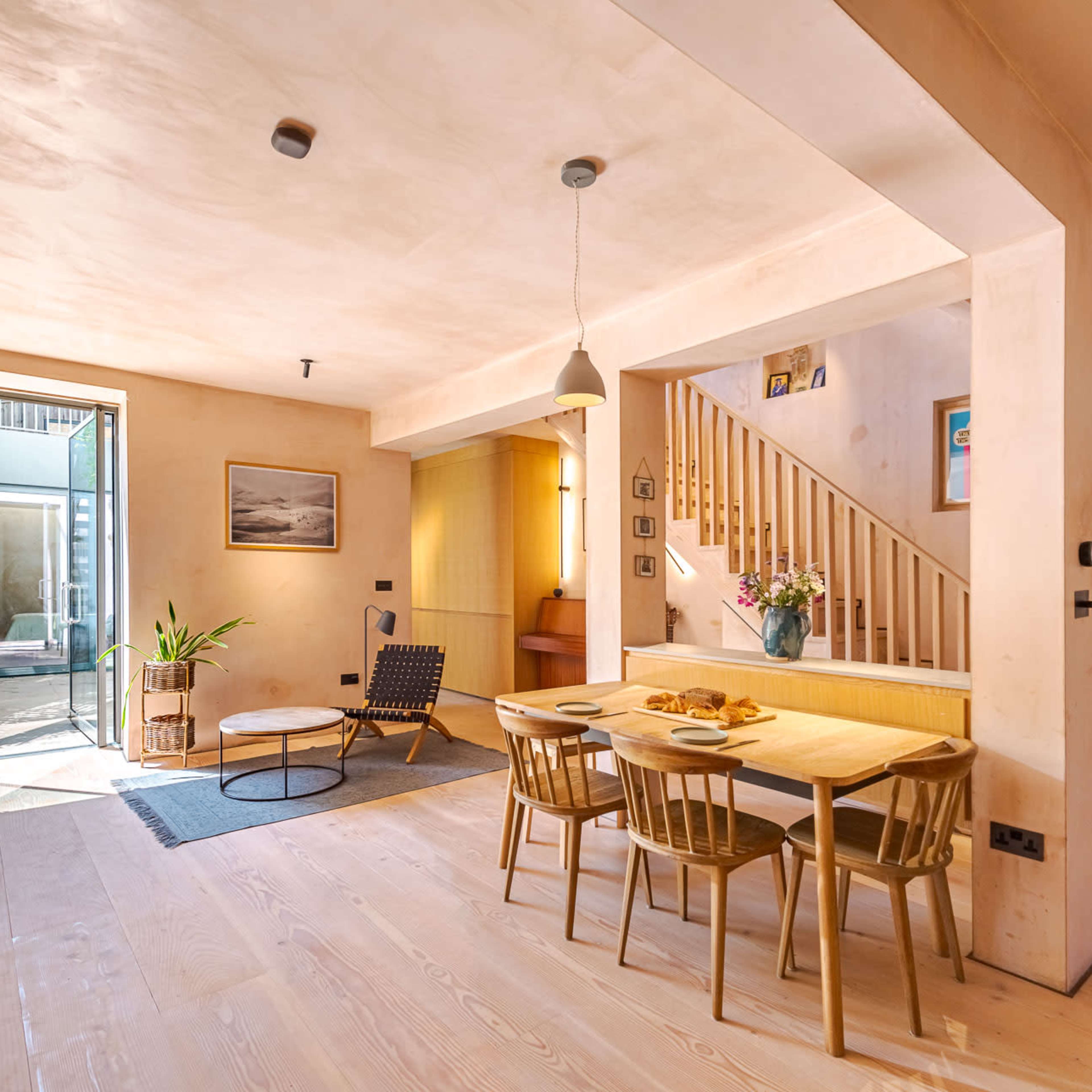 A modern open-plan living space with a dining area, a staircase, and large windows leading to an outdoor garden.