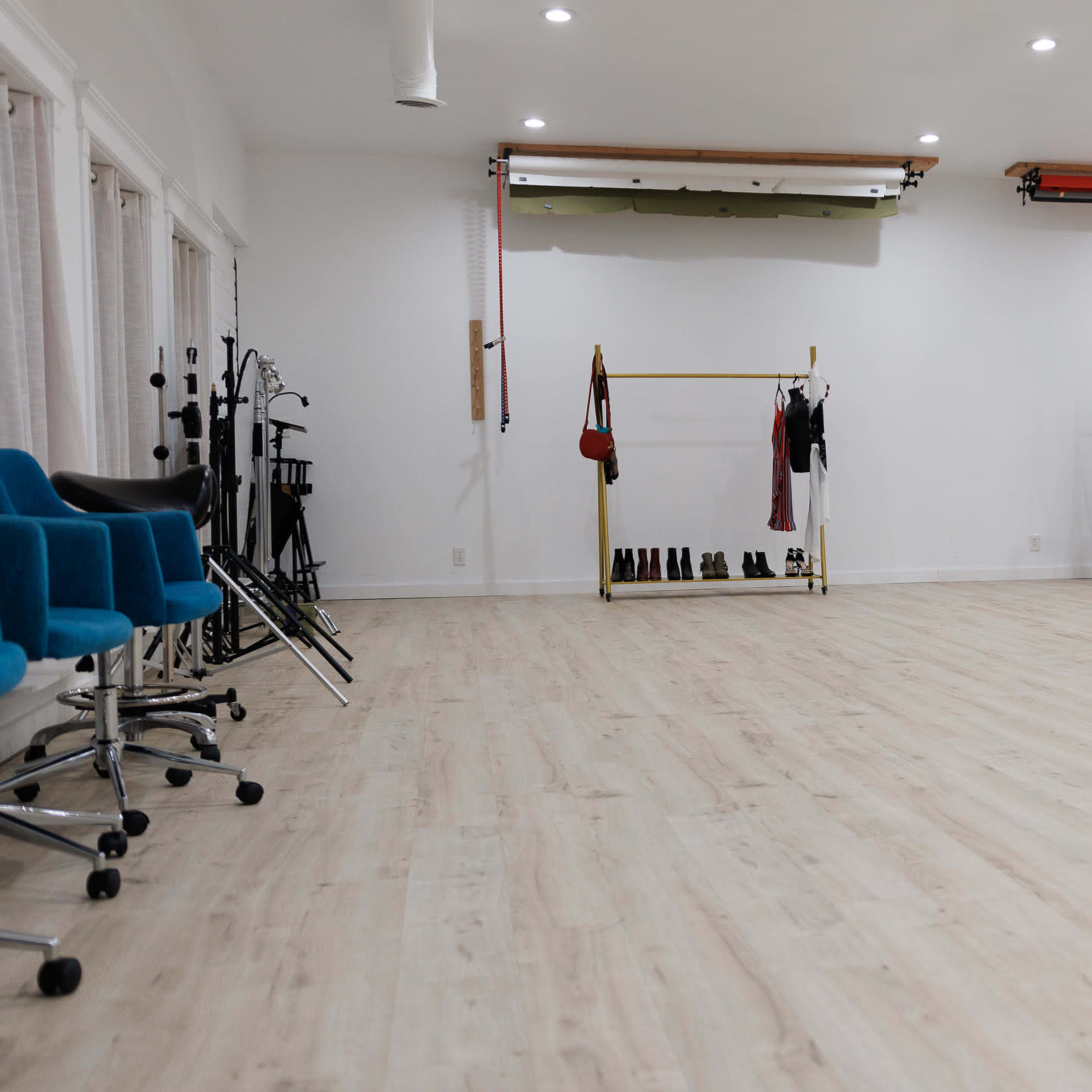 A spacious, well-lit studio with a wooden floor, clothing racks displaying garments, and colorful chairs arranged on one side.