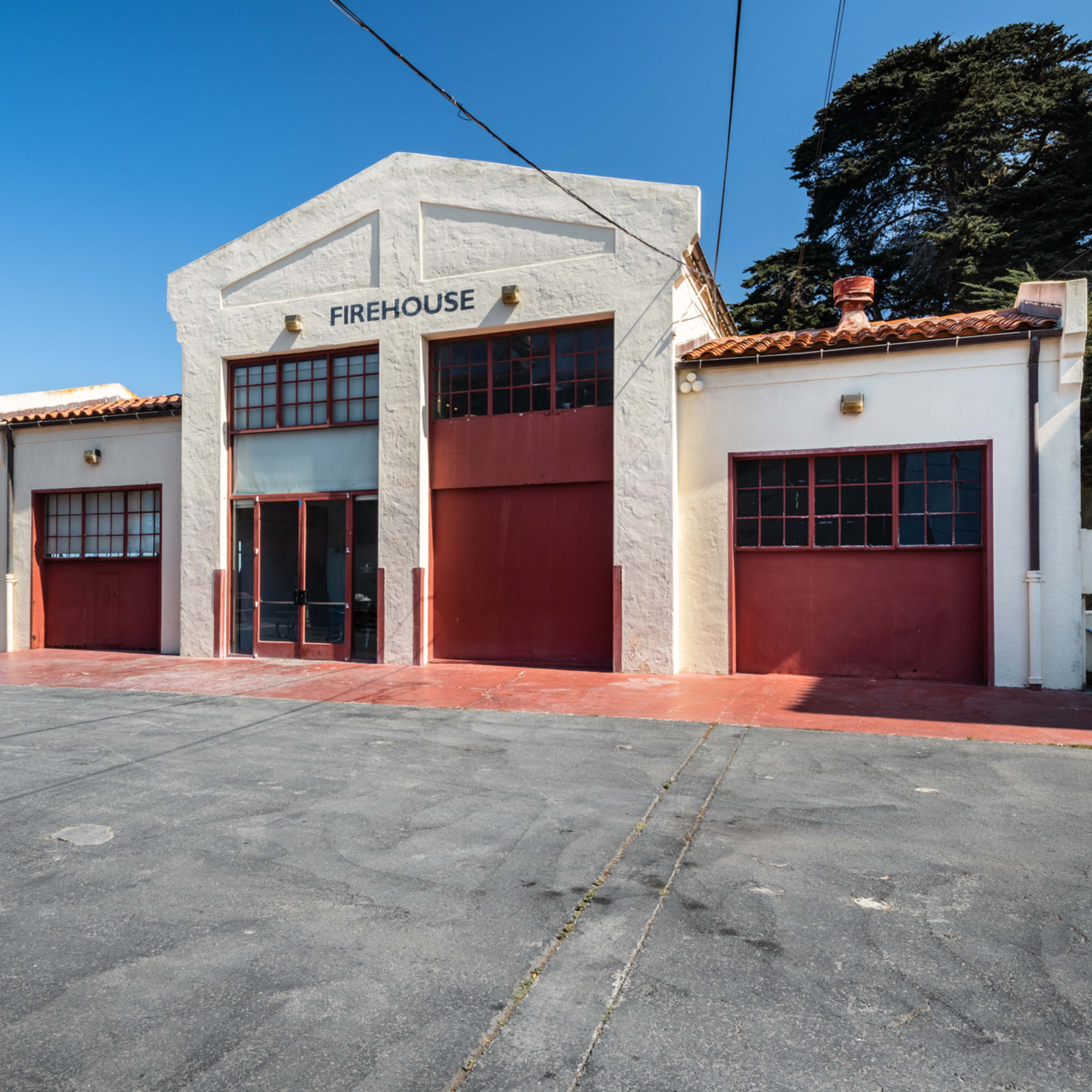 A firehouse building with a flat roof, two large red doors, and a view of the water in the background.