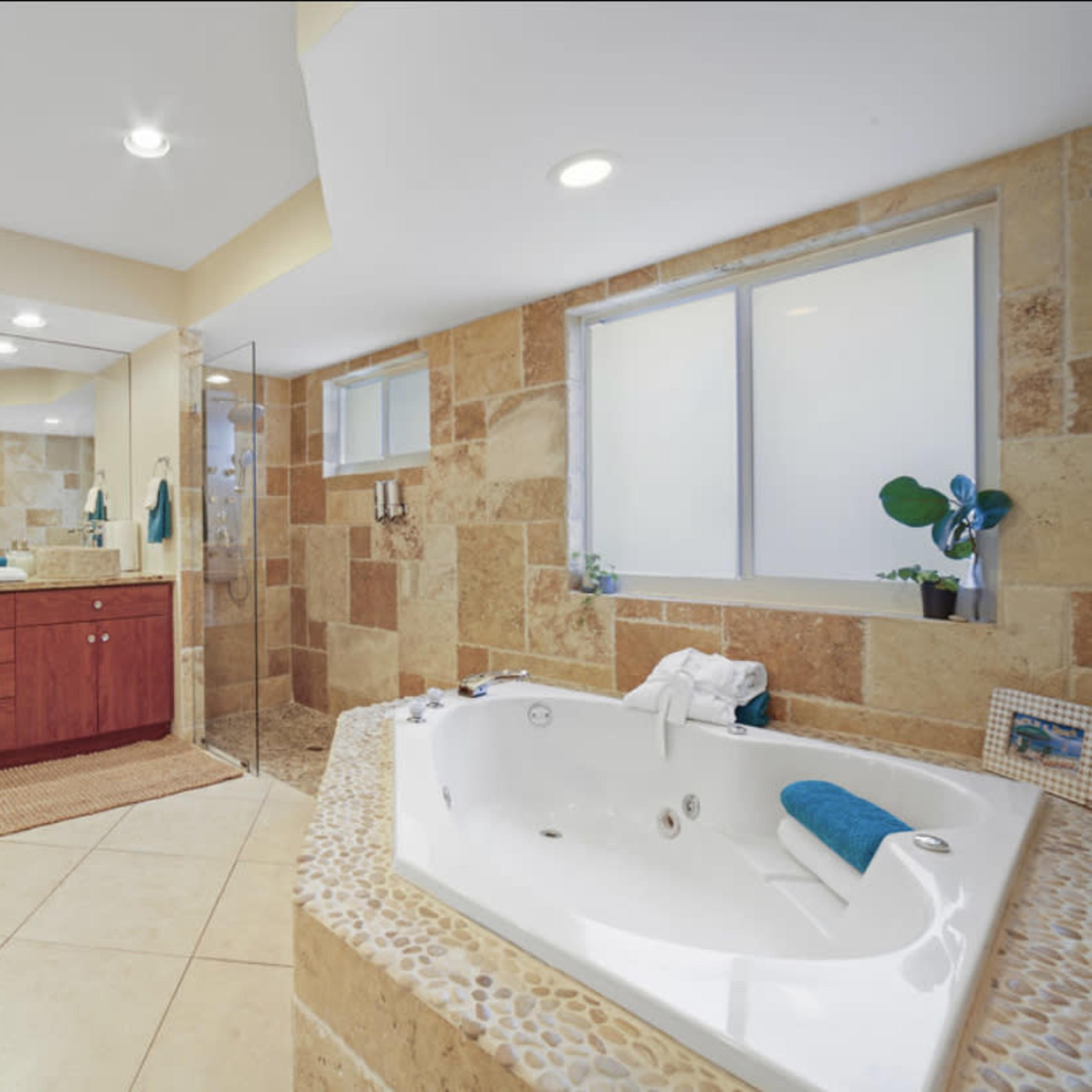 A spacious bathroom featuring a jetted tub, a double vanity with red cabinets, a walk-in shower, and stone tile accents.