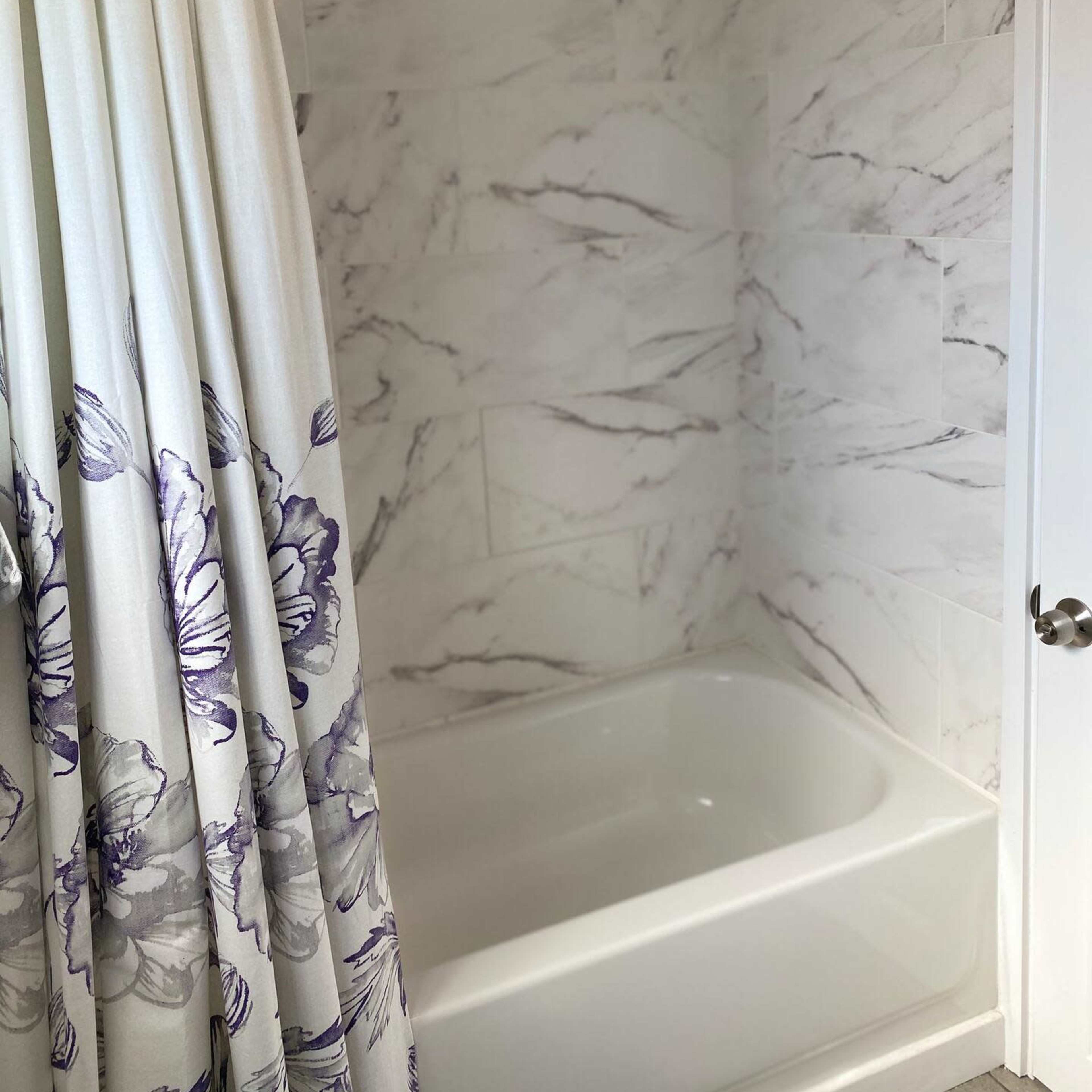 A bathroom with a shower area featuring a white tub and a floral shower curtain against marble-patterned walls.