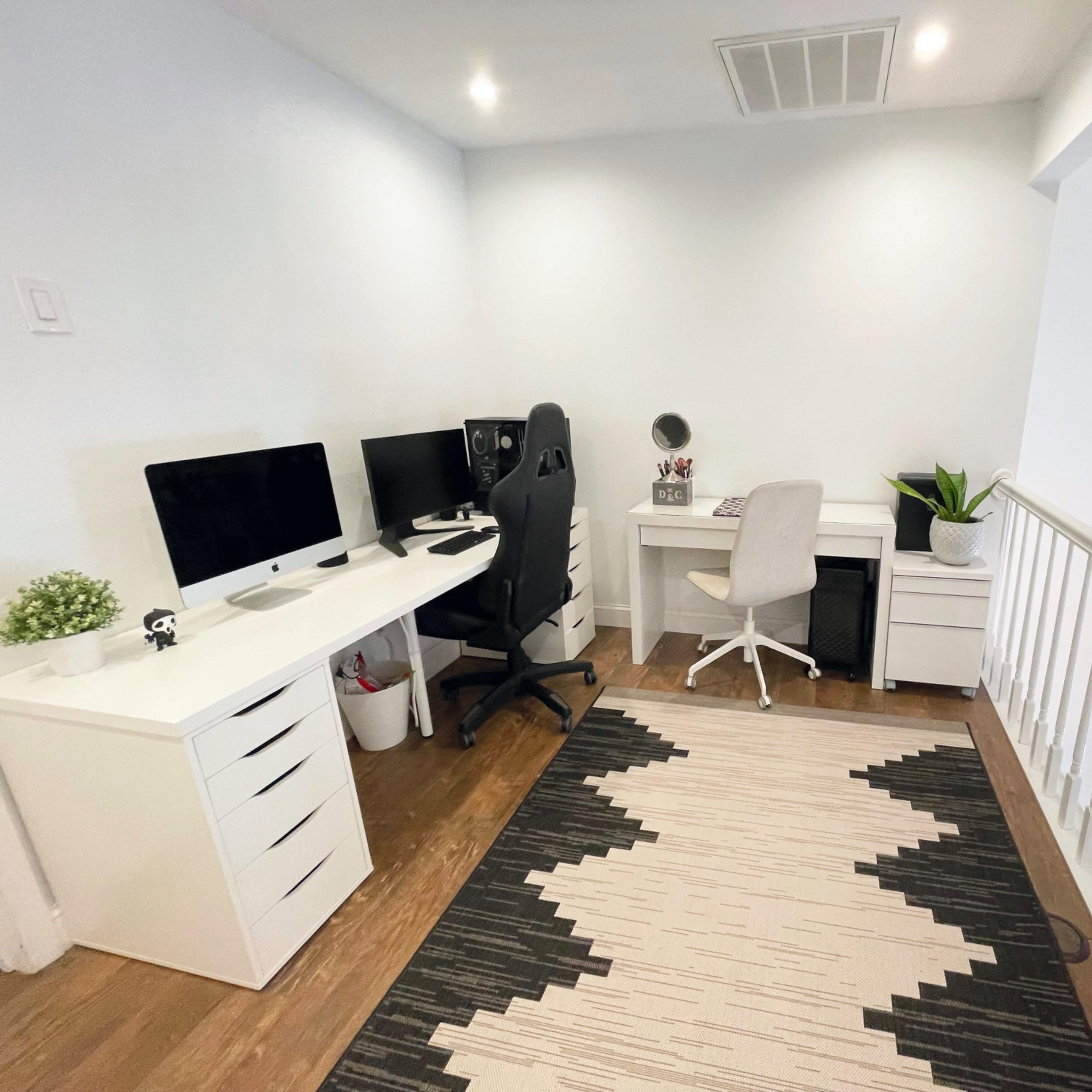 A modern home office setup with two desks, an ergonomic chair, a computer, and a decorative plant near a staircase.