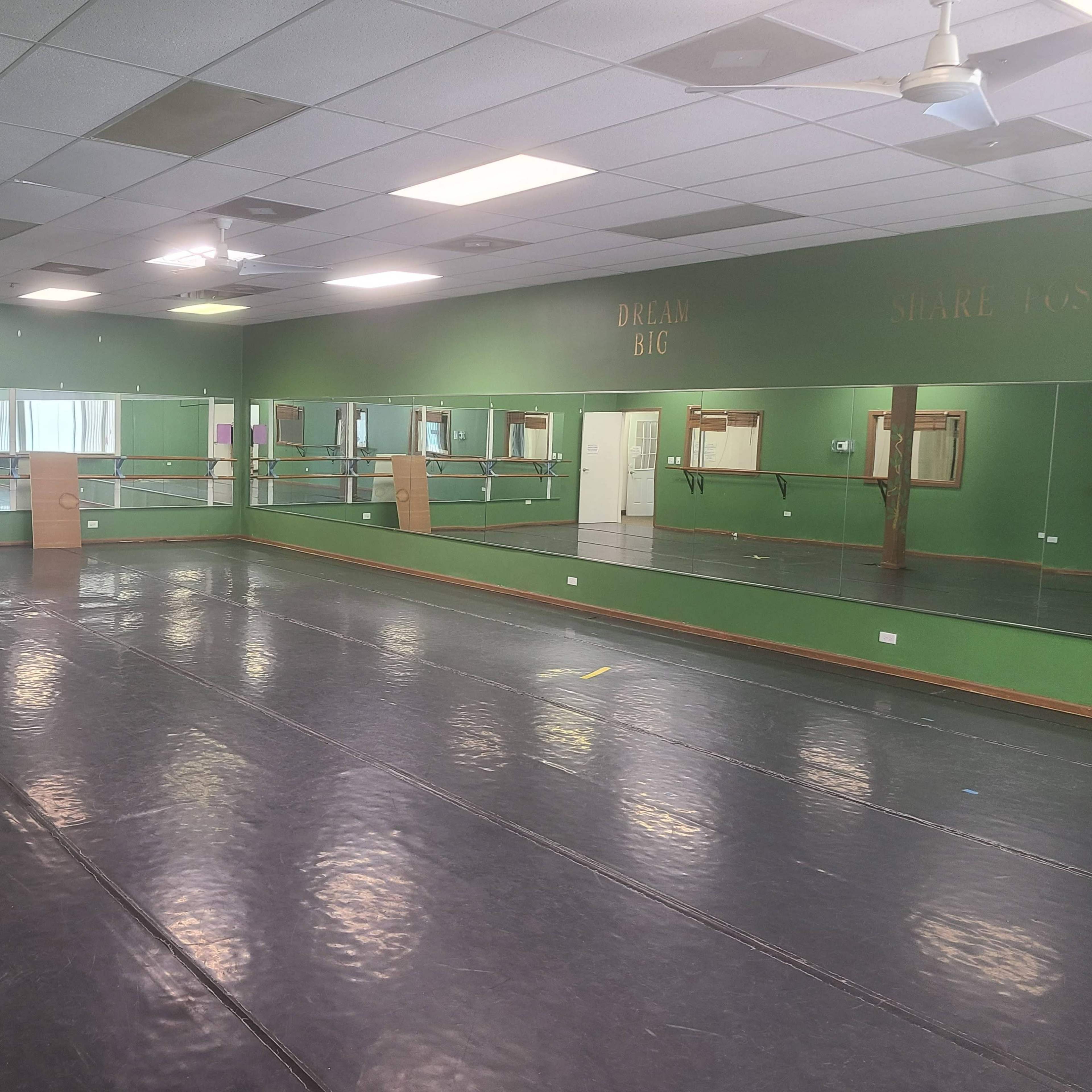 A spacious dance studio with mirrored walls, a wood barre, and a gray floor.