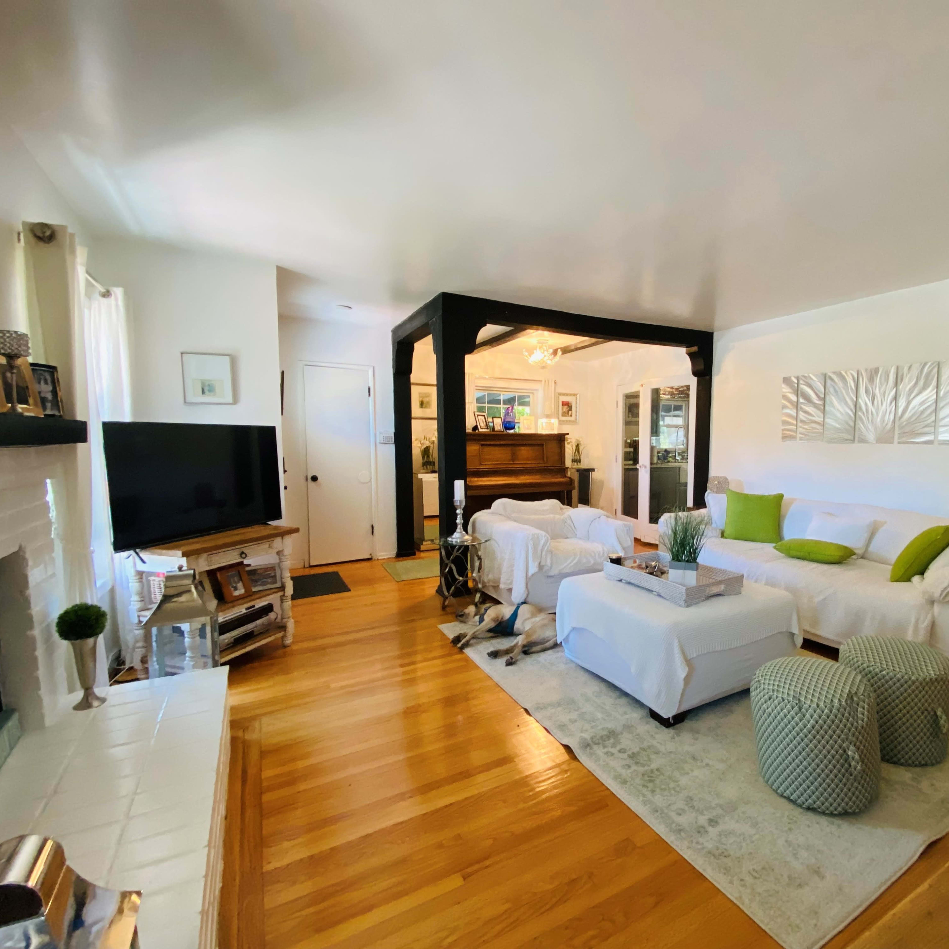 A bright living room with a white sofa, a coffee table, and a piano in the background, situated on wooden flooring.