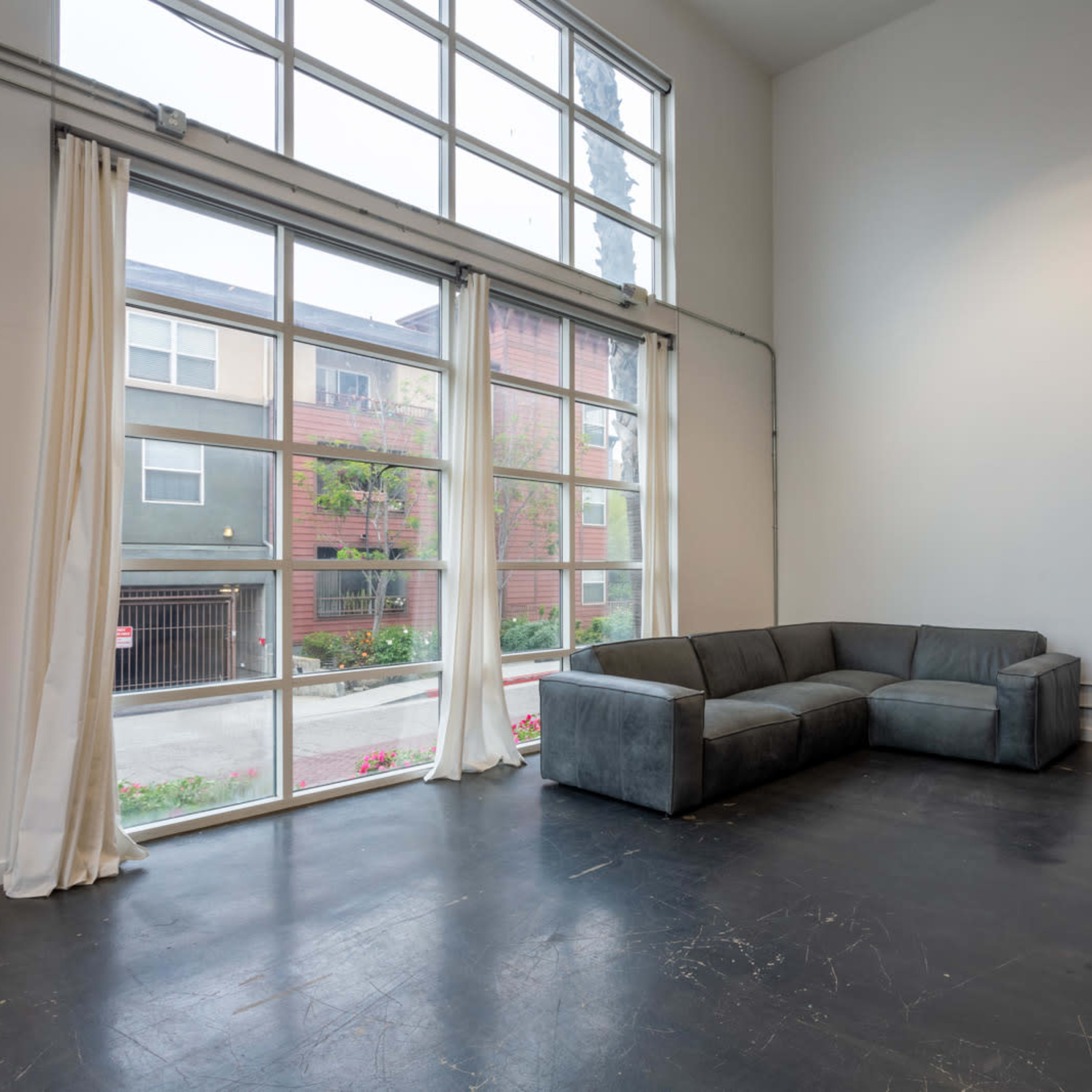 A spacious interior with a large window, featuring a gray sectional sofa in a corner against a blank wall.