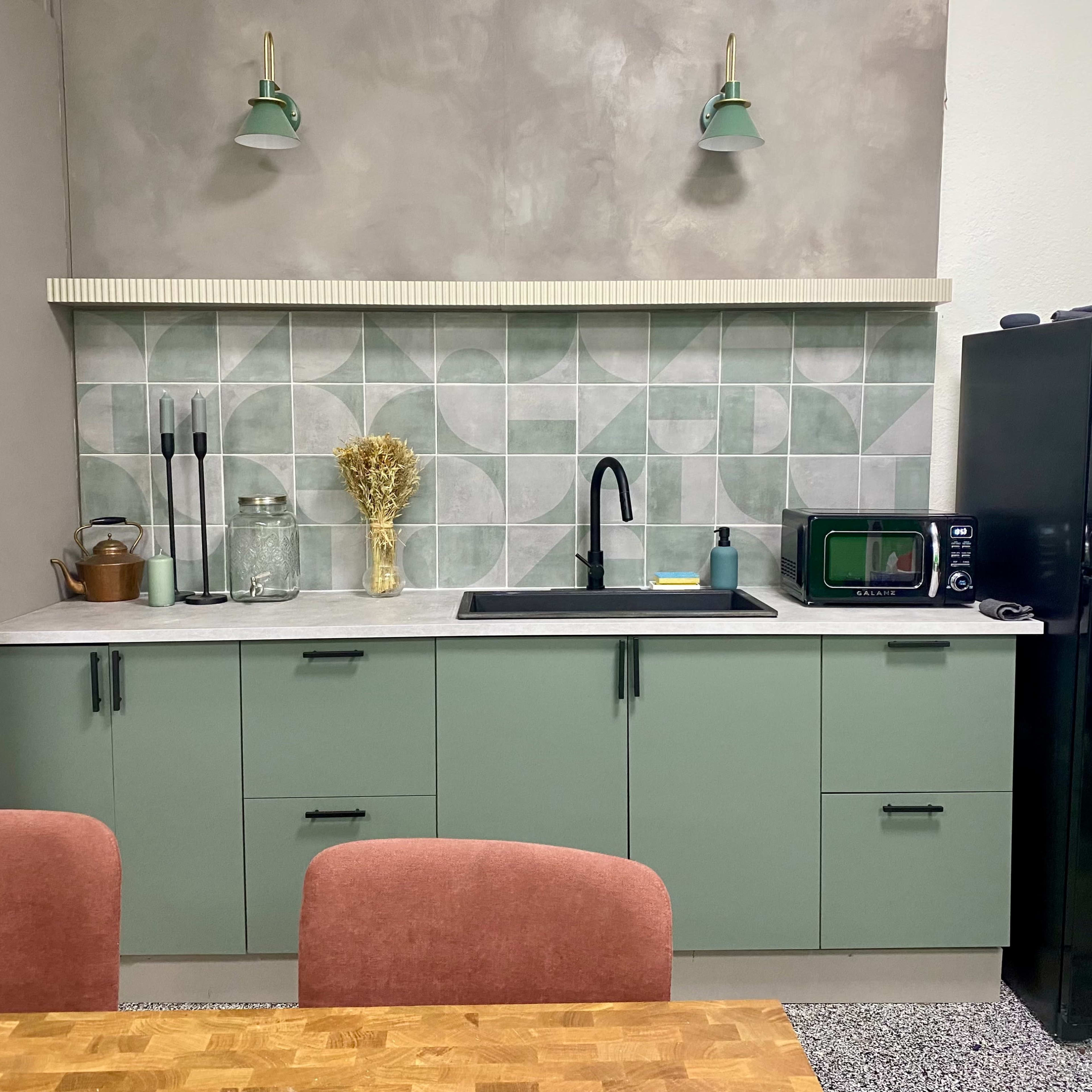 A modern kitchen with green cabinets, a black sink, and a countertop featuring a patterned backsplash.