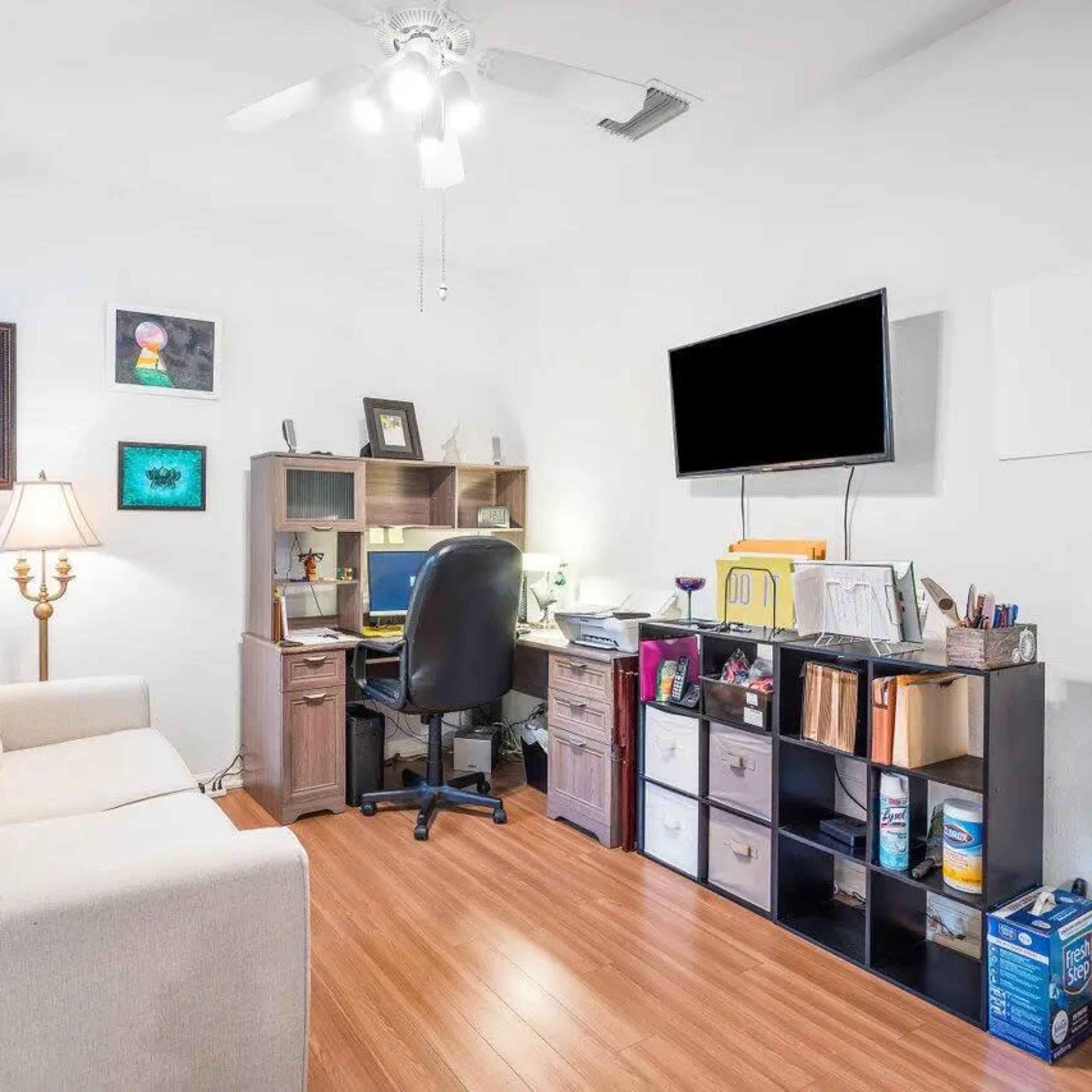 A small, organized office space featuring a desk with a computer, a comfortable couch, and a shelving unit filled with various items.