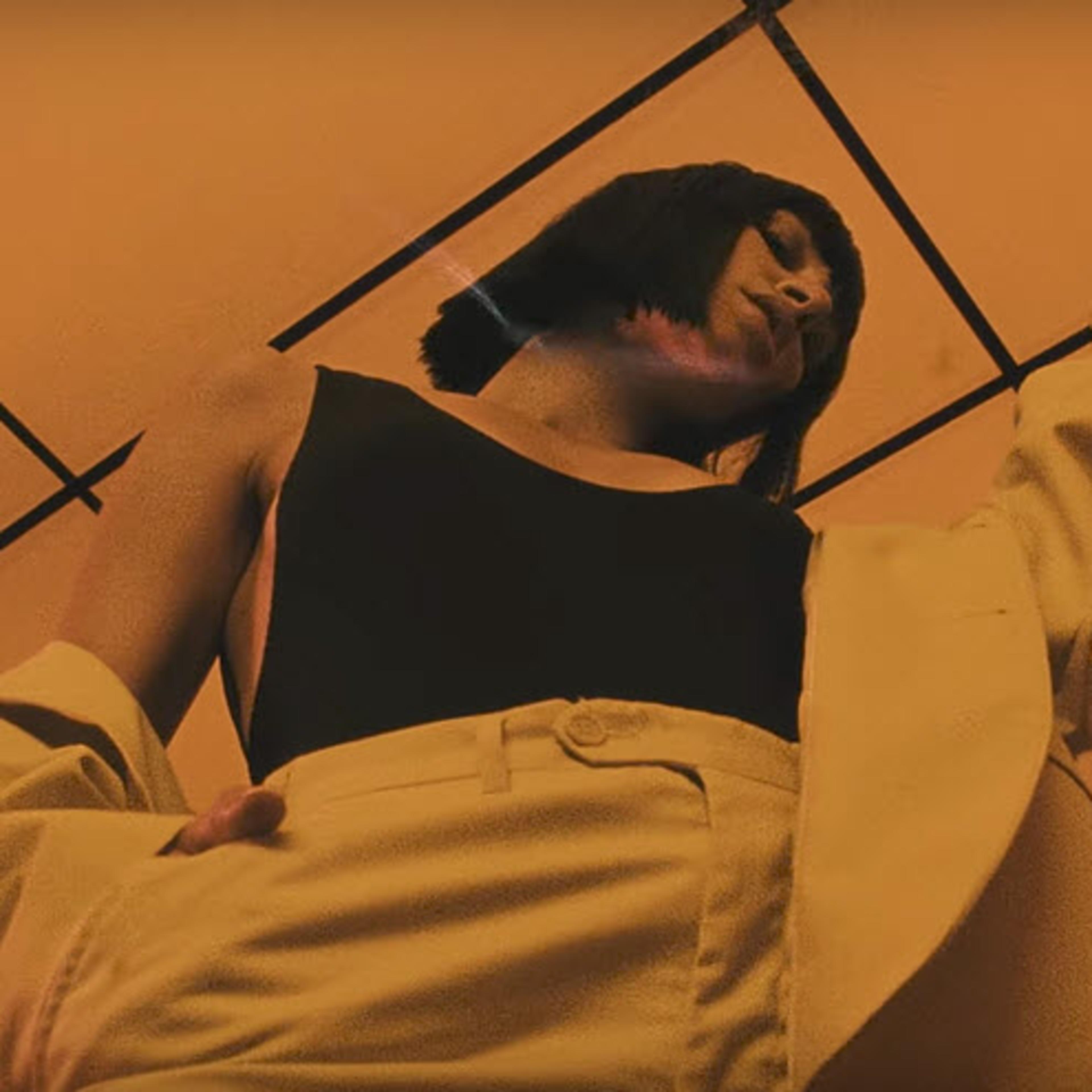 A person in a black shirt and light-colored pants poses beneath an orange-tinted ceiling.