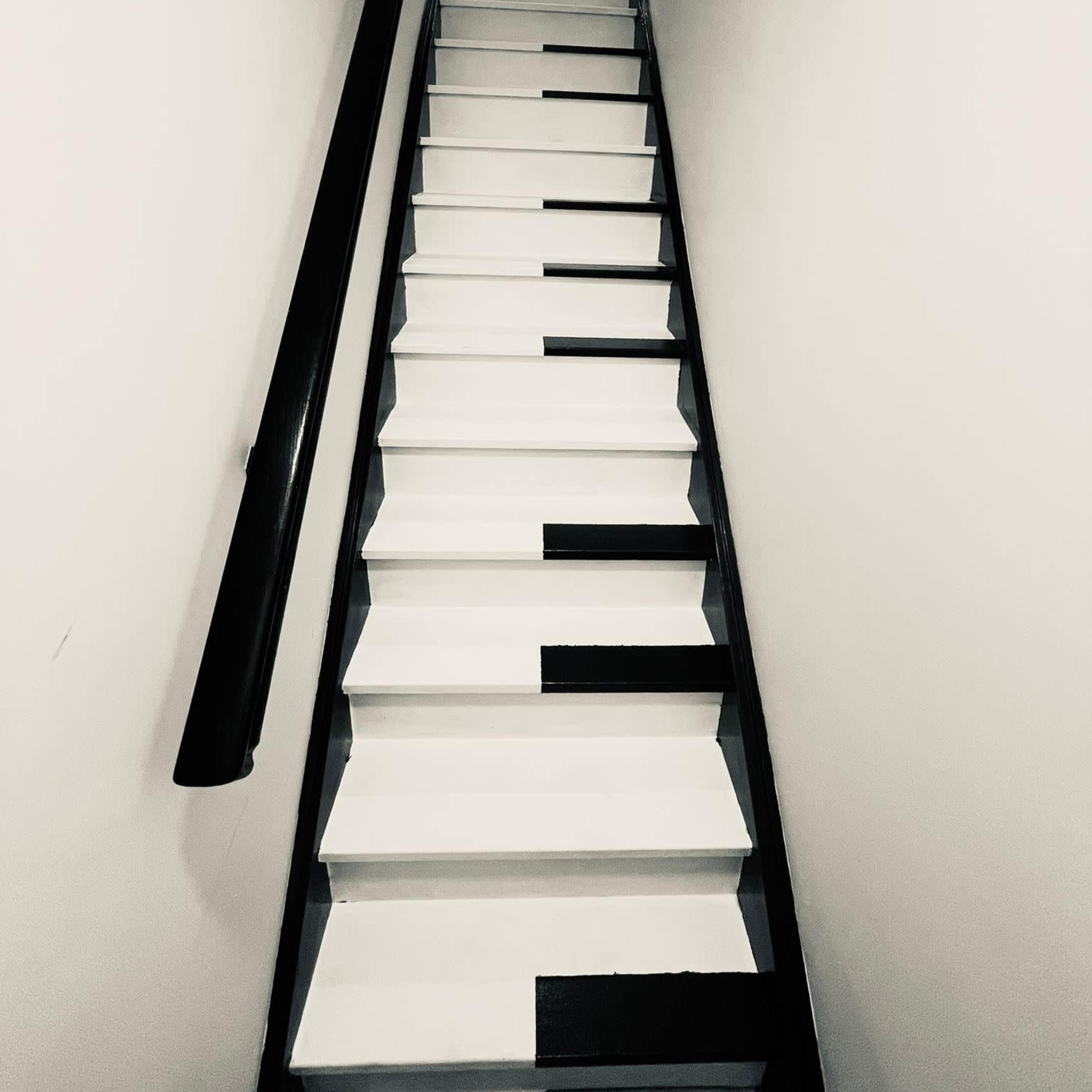 A staircase with steps painted to resemble a piano keyboard ascends into a well-lit hallway.