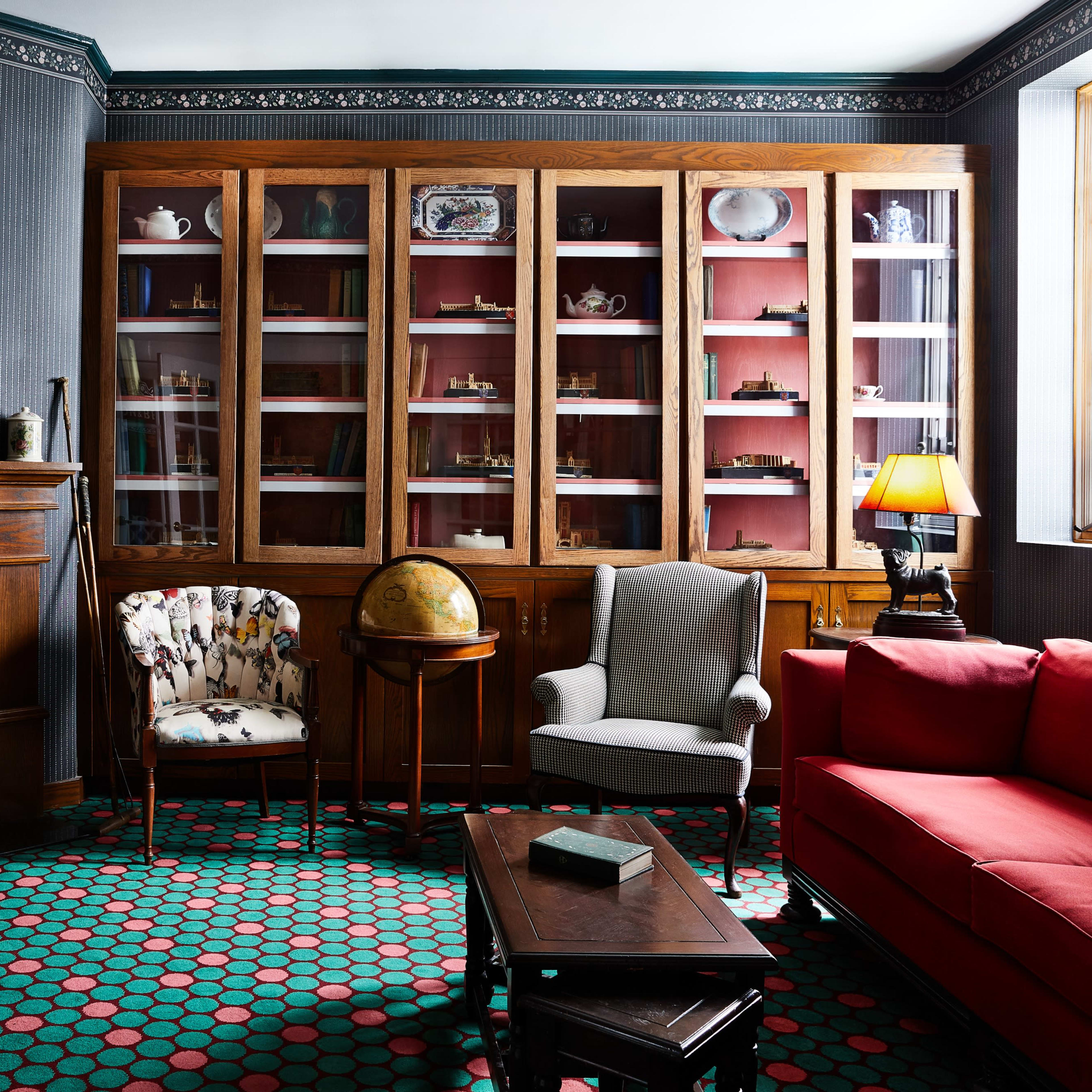 A vintage living room with a fireplace, a bookshelf containing various collectibles, and patterned carpet.