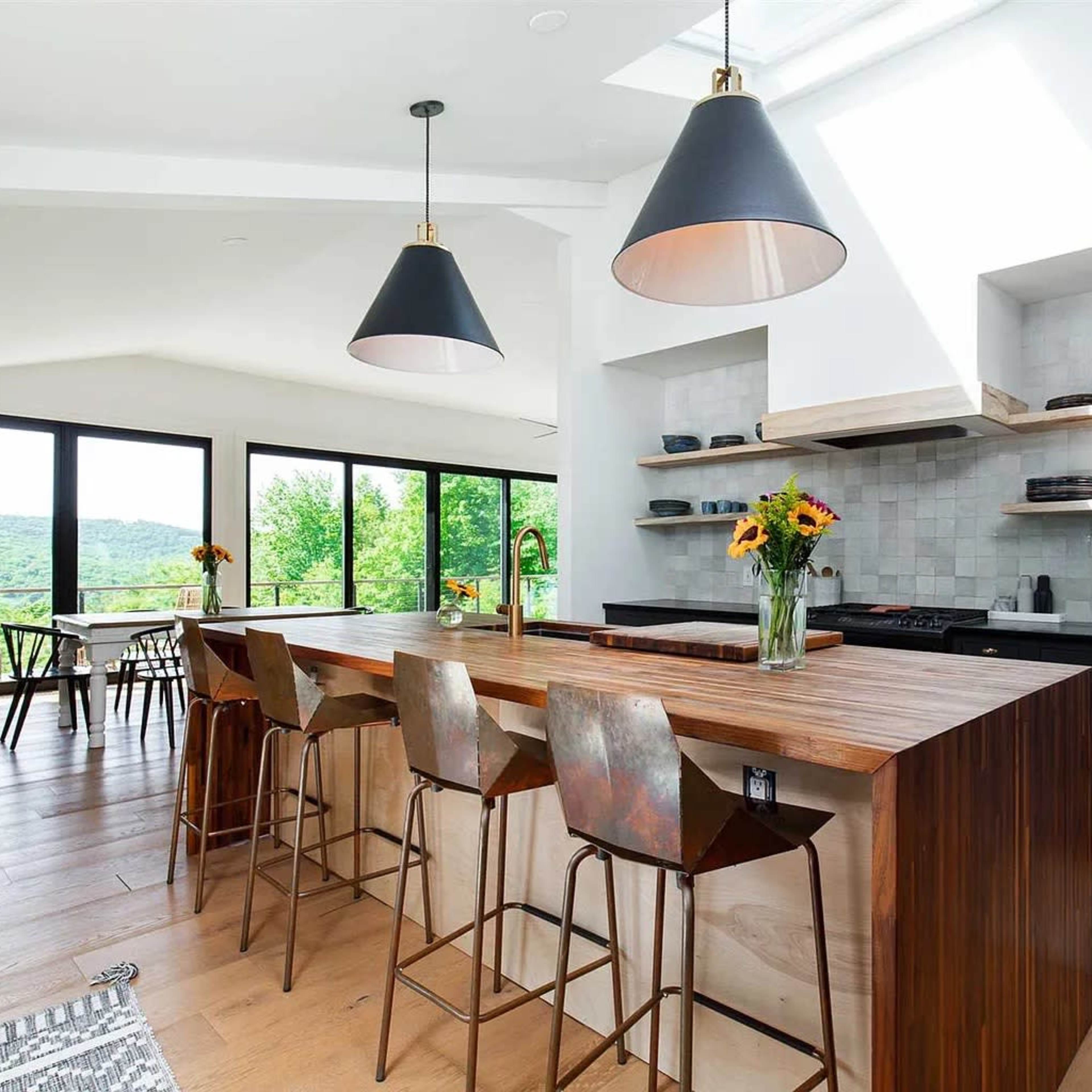 A modern kitchen features a large wooden island with bar stools, open shelving, and a panoramic view through expansive windows.
