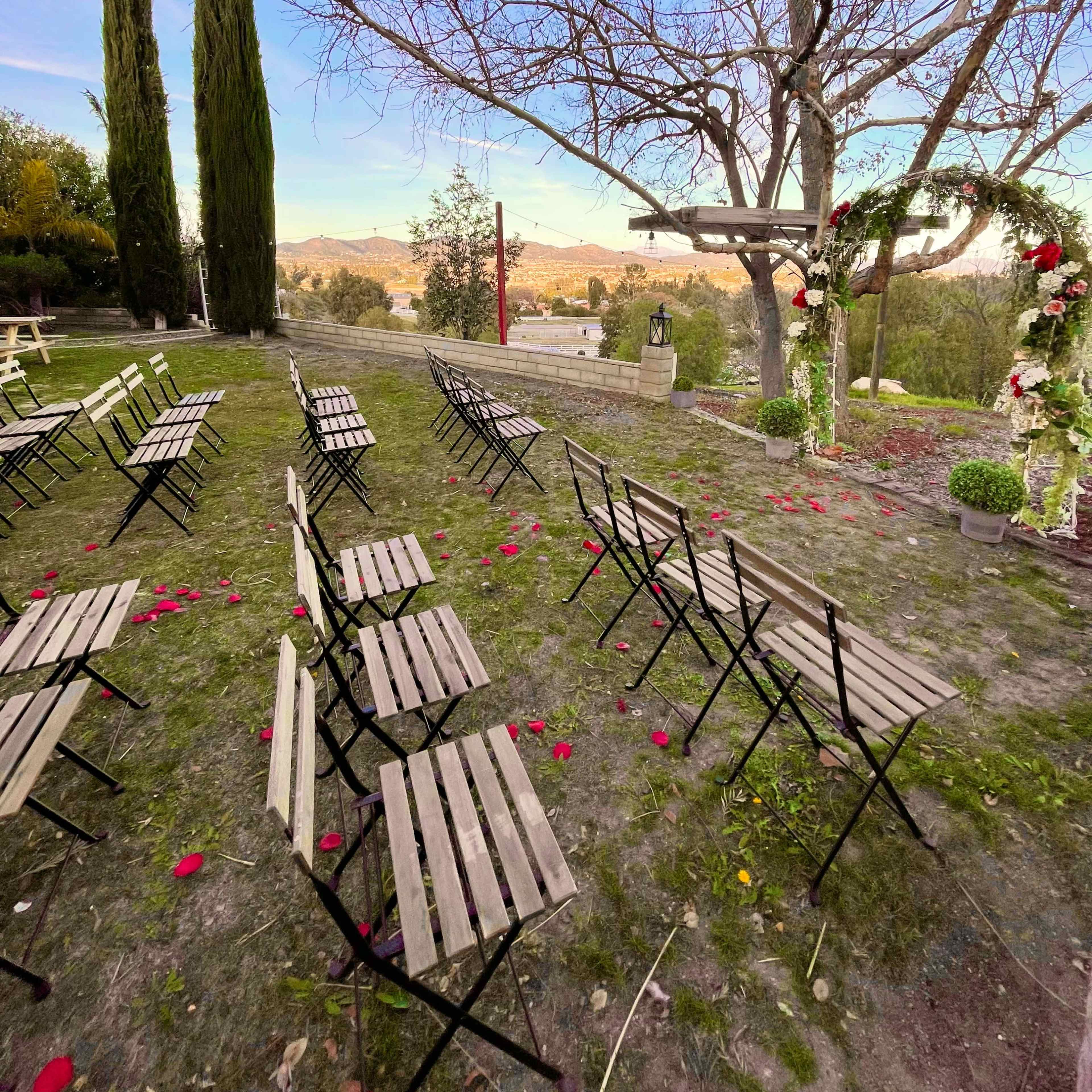 A covered outdoor seating area with white sofas and wooden tables, surrounded by greenery.