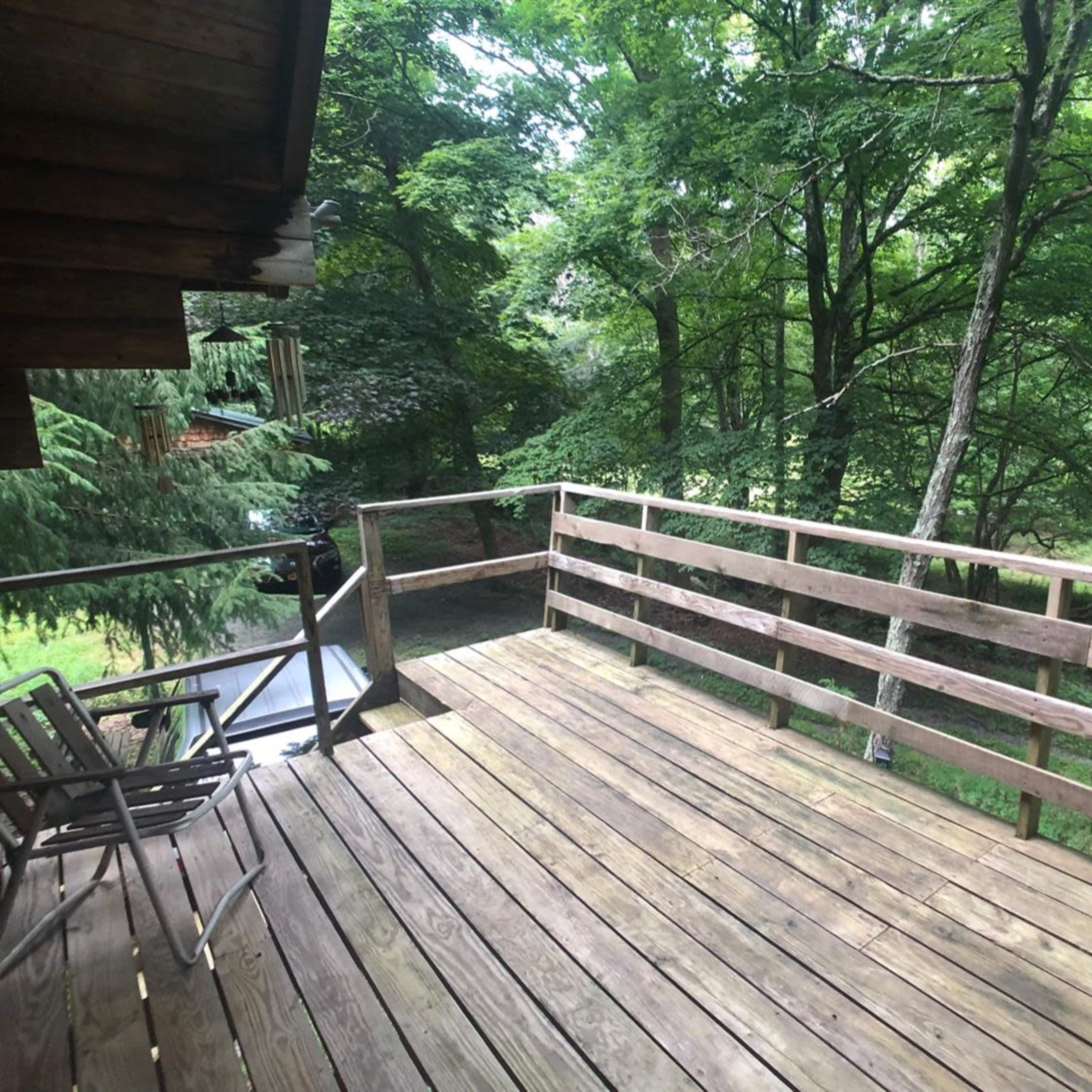 A wooden deck with chairs overlooks a densely wooded area.